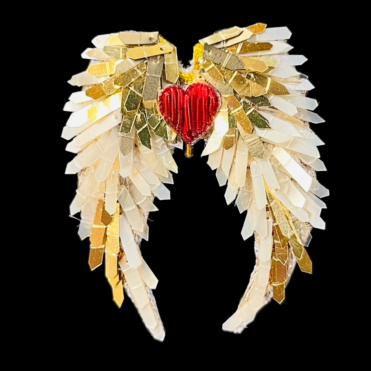 A handmade angel wing brooch featuring layered white and gold metallic paper wings with a central red beaded heart, displayed on a black background.
