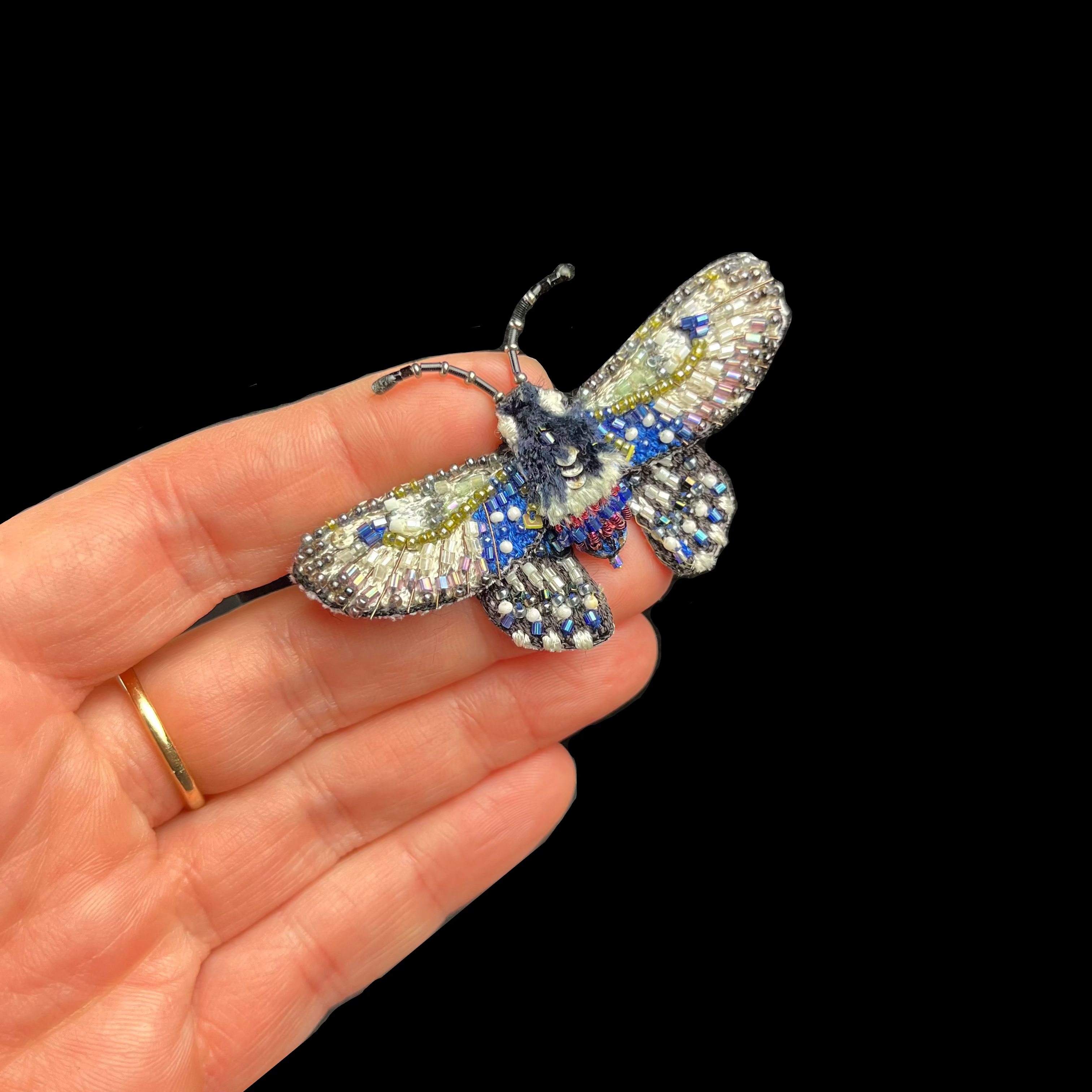 Hand holding a butterfly-shaped brooch with gemstones on a dark background