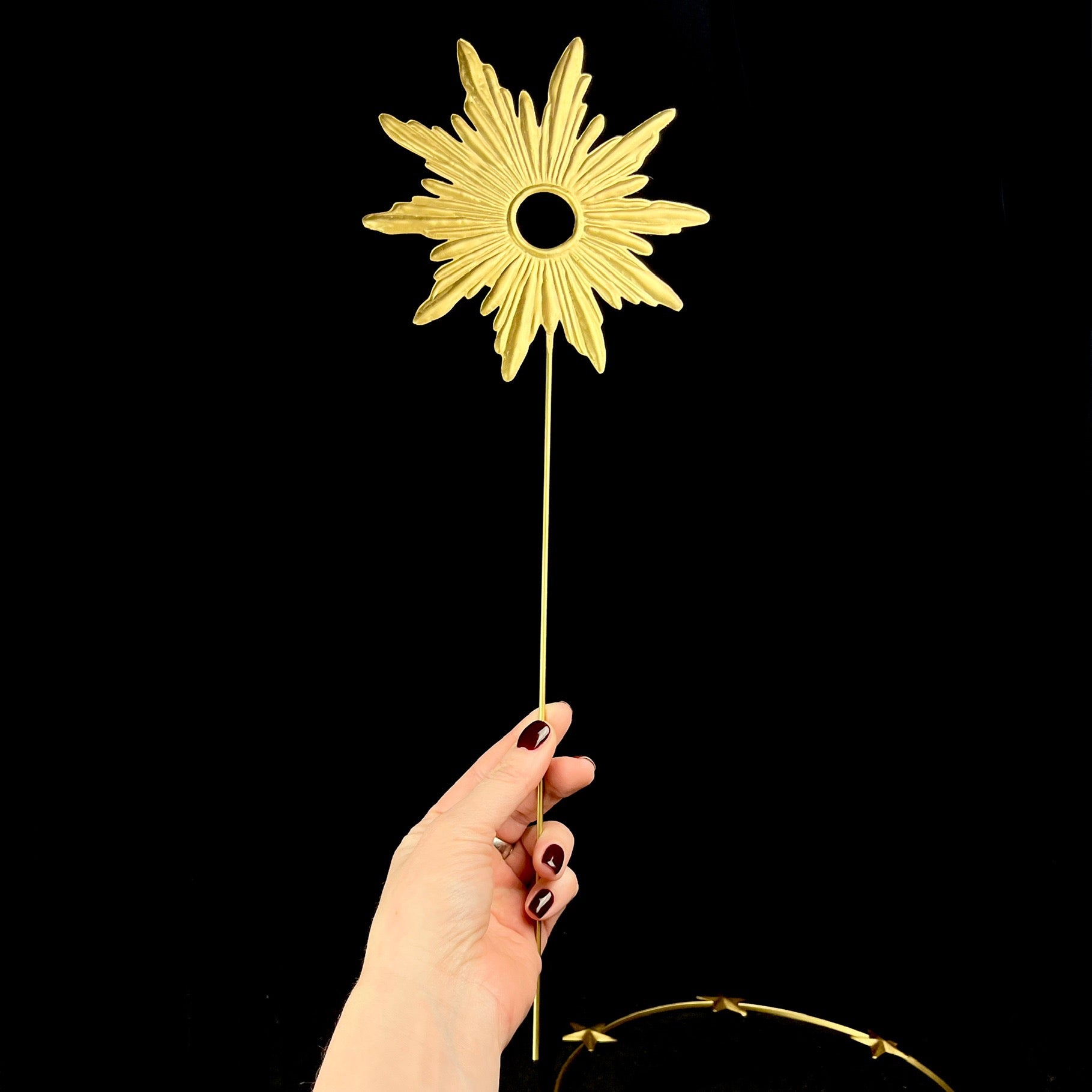 Golden rays around open circular center attached to thin dowel shown held in hand