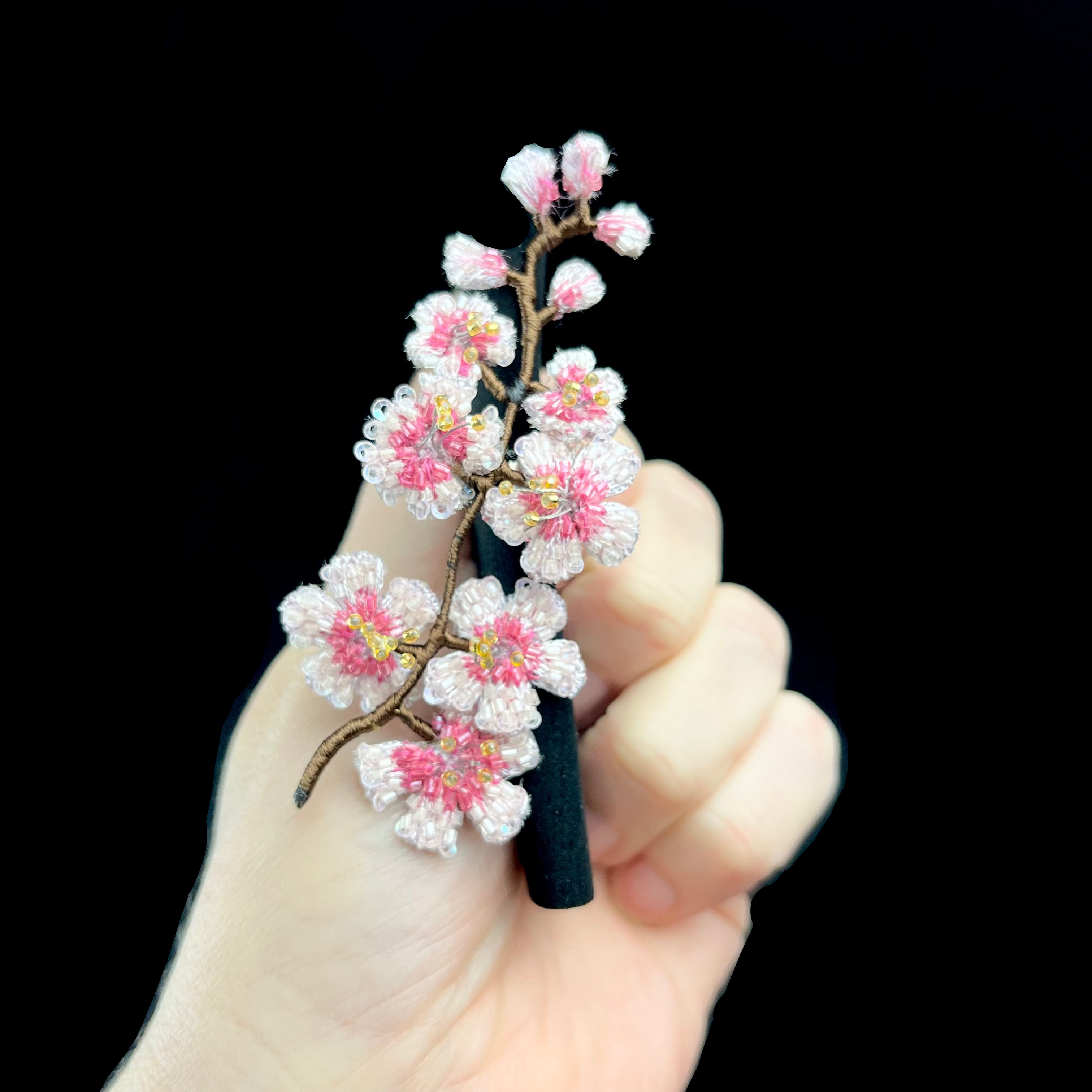 Hand holding a decorative hairpin with pink floral design against a dark background