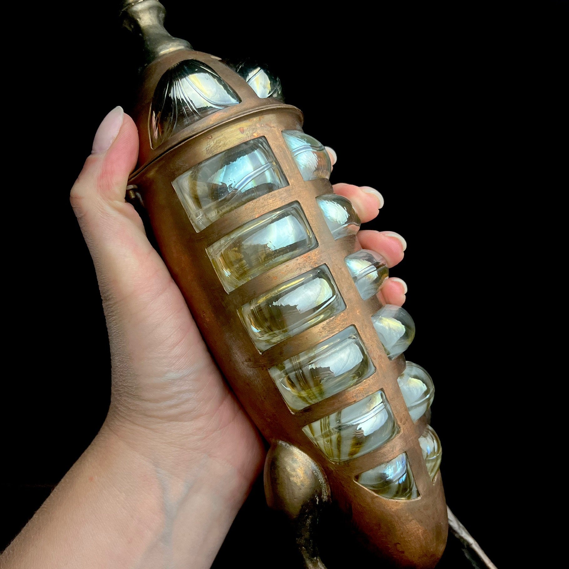 Hand holding a vintage-style light fixture with glass panels against a black background