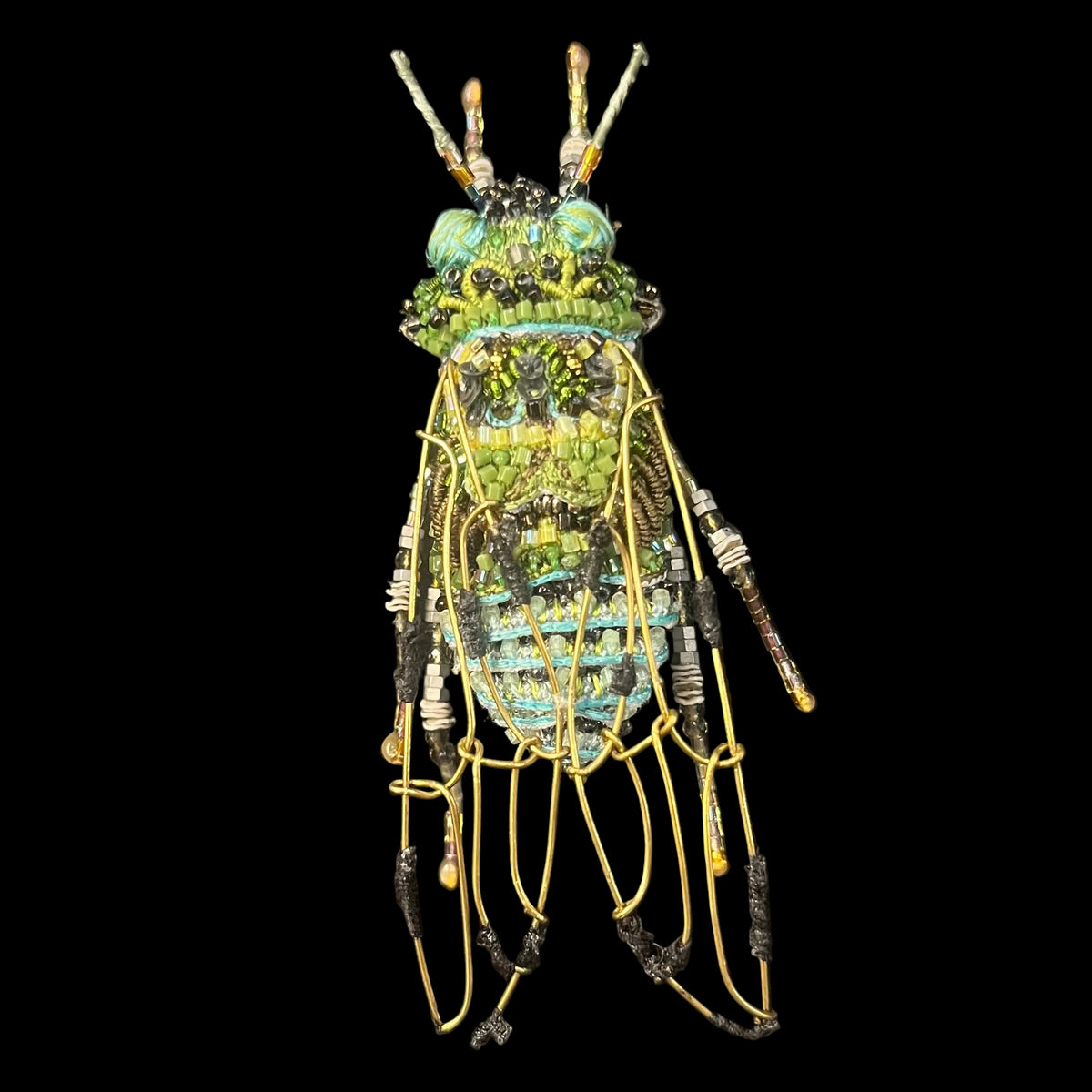 Bent brass wire wings stand above a fabric embroidered bug body with glitteringly glass beads of blue and green