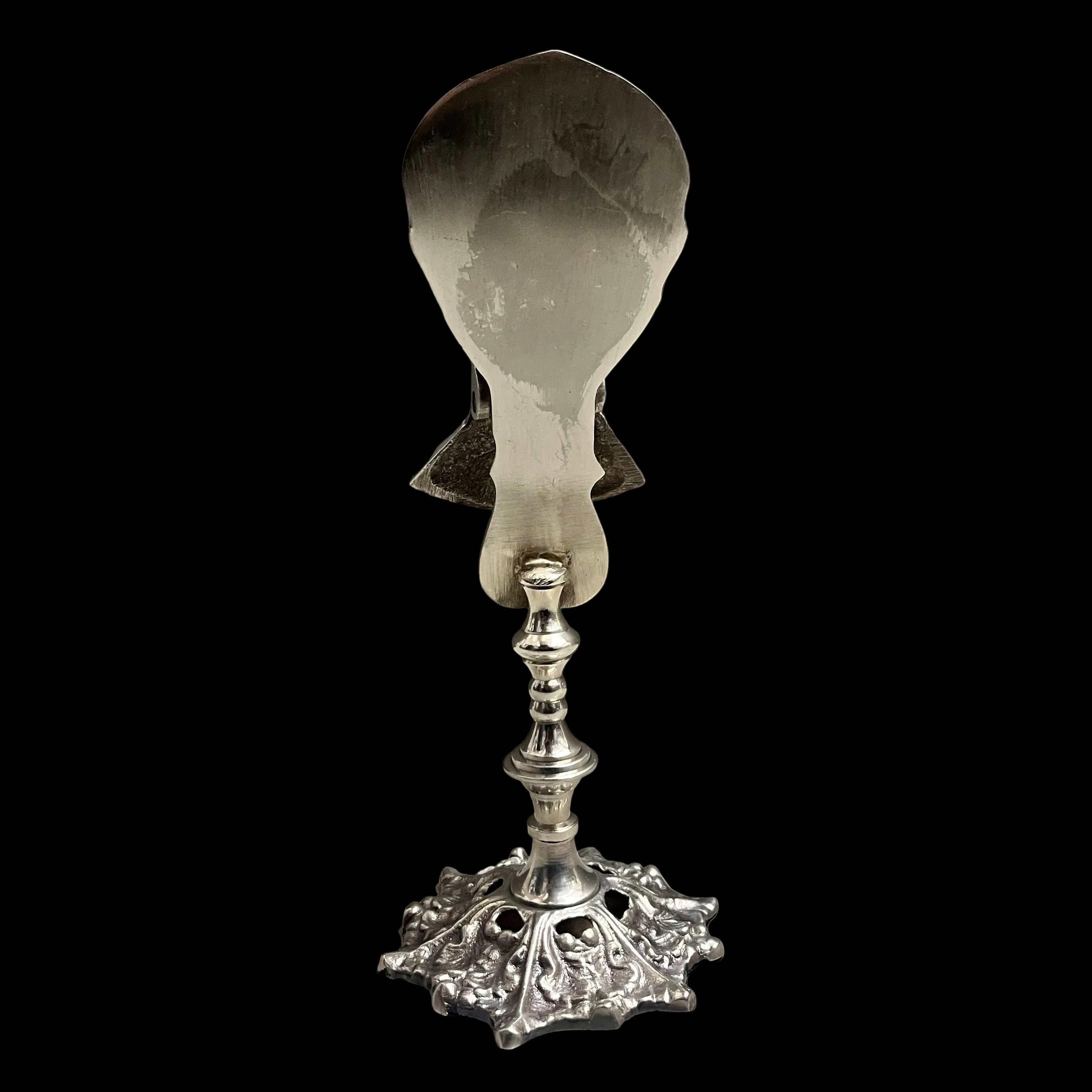 Decorative silver spoon holder with a decorative base on a gray background