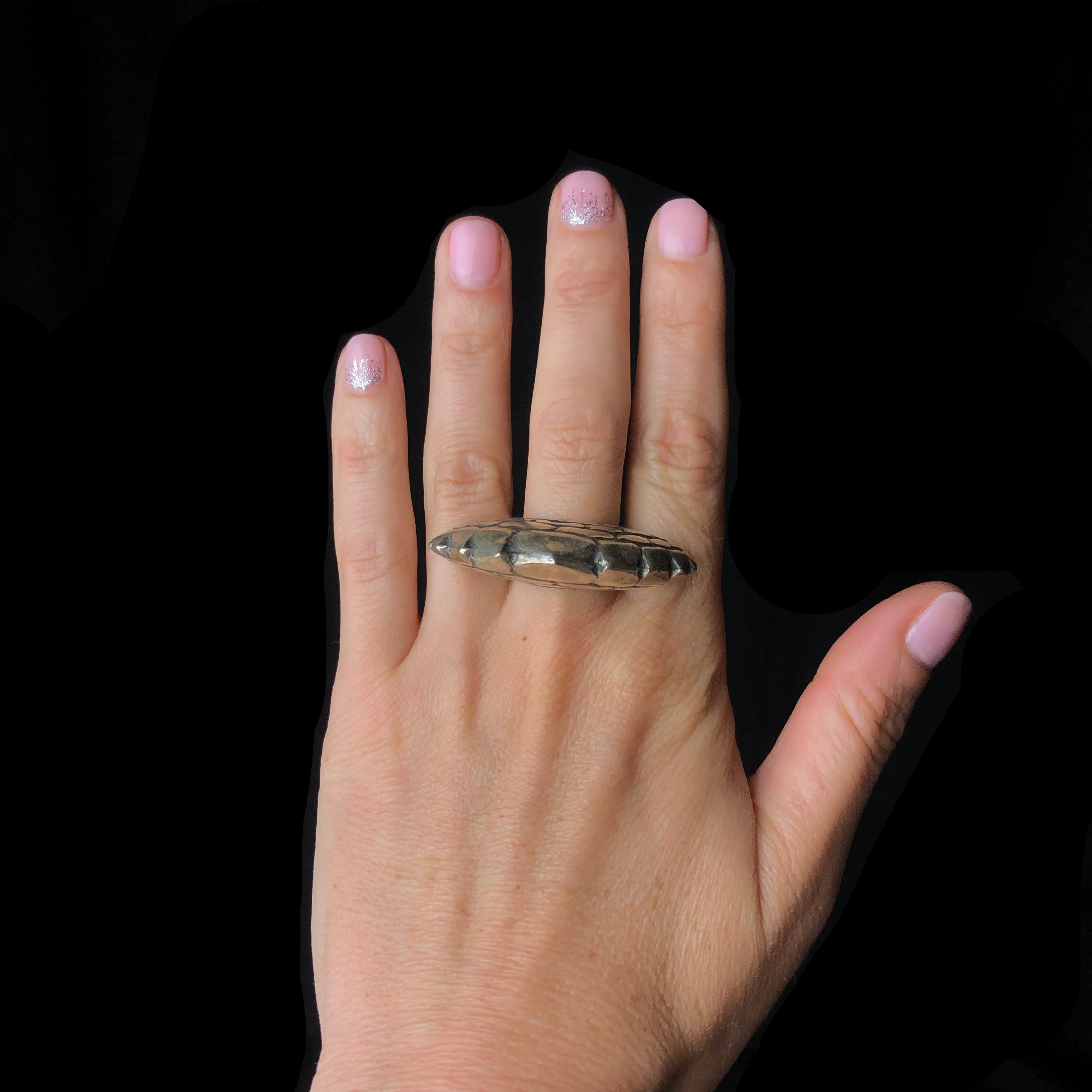 Hand wearing a silver ring with pink nail polish on a black background