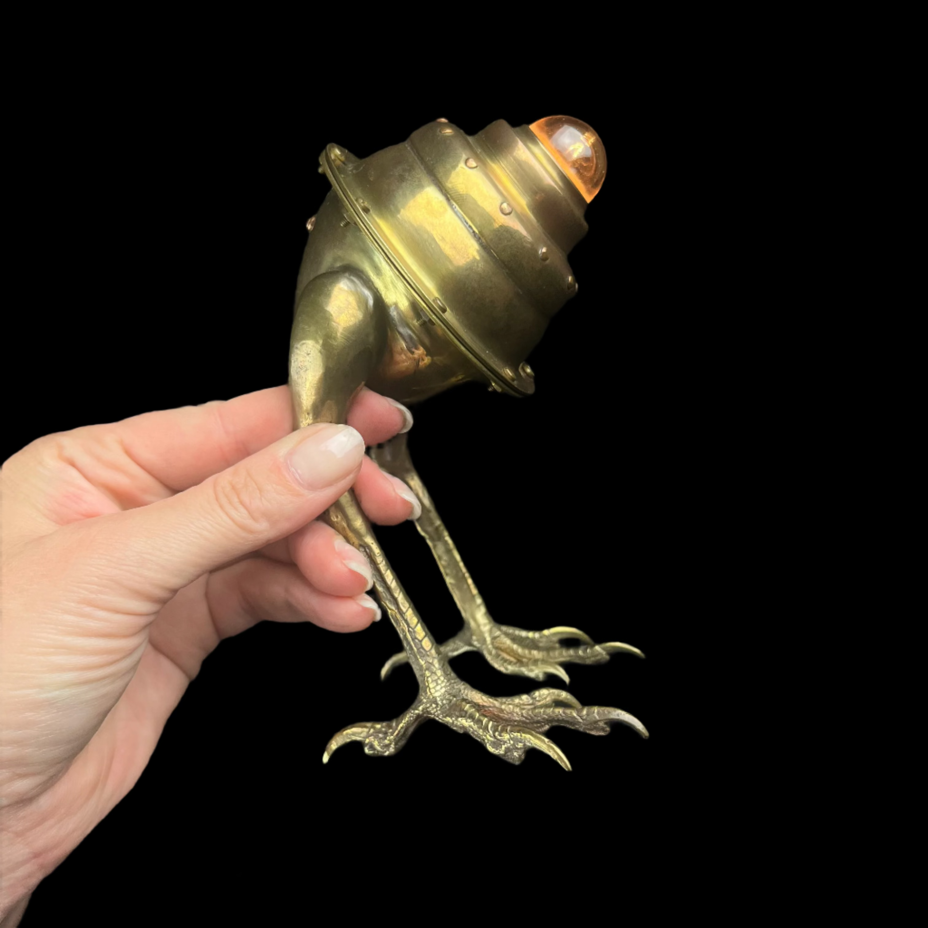 Hand holding a brass frog-shaped lamp against a dark background