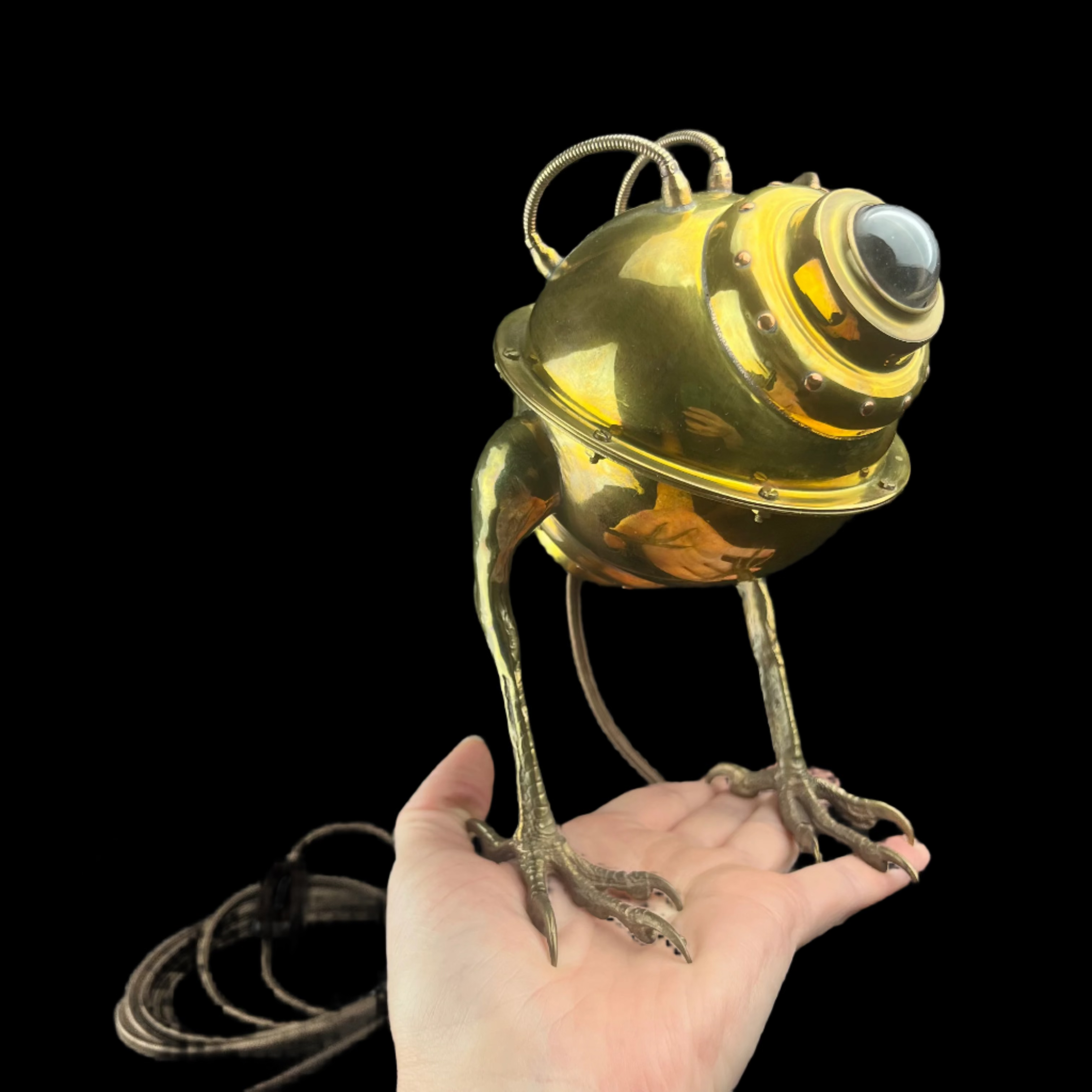 Gold robot-like lamp held in a hand against a dark background