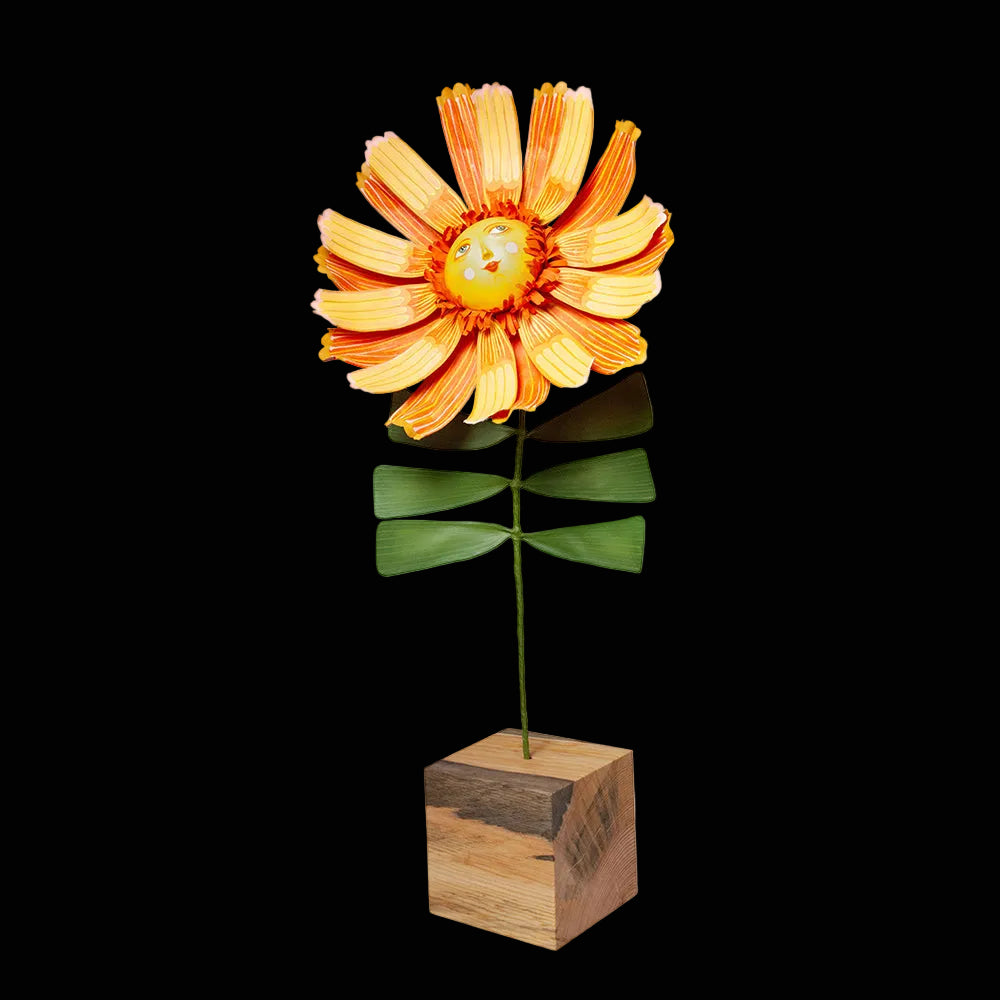 Bright yellow and orange flower sculpture with a smiling face in the center turned up petals standing a green stem with square wooden base.