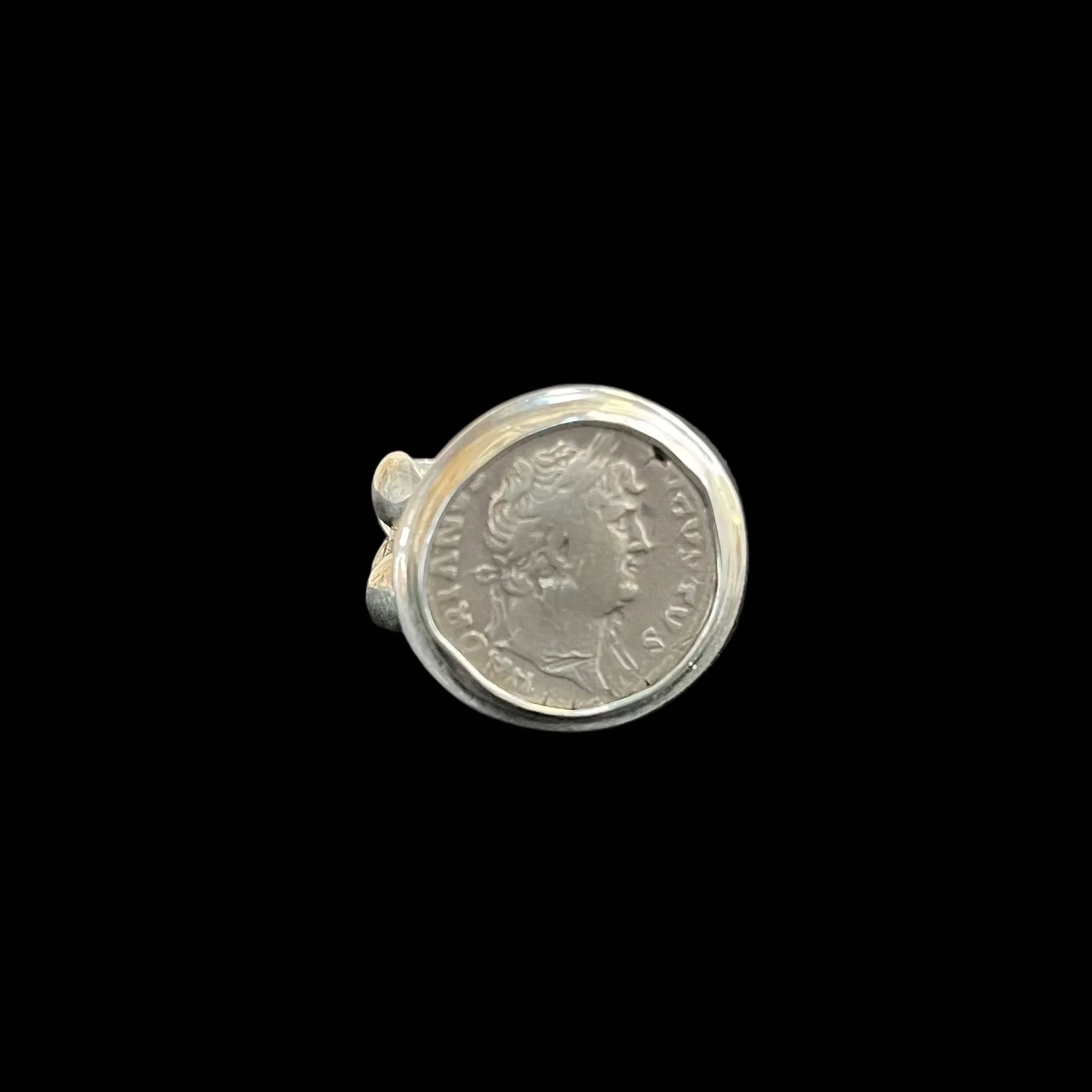 Silver ring with a coin design on a black surface, blurred brick wall background
