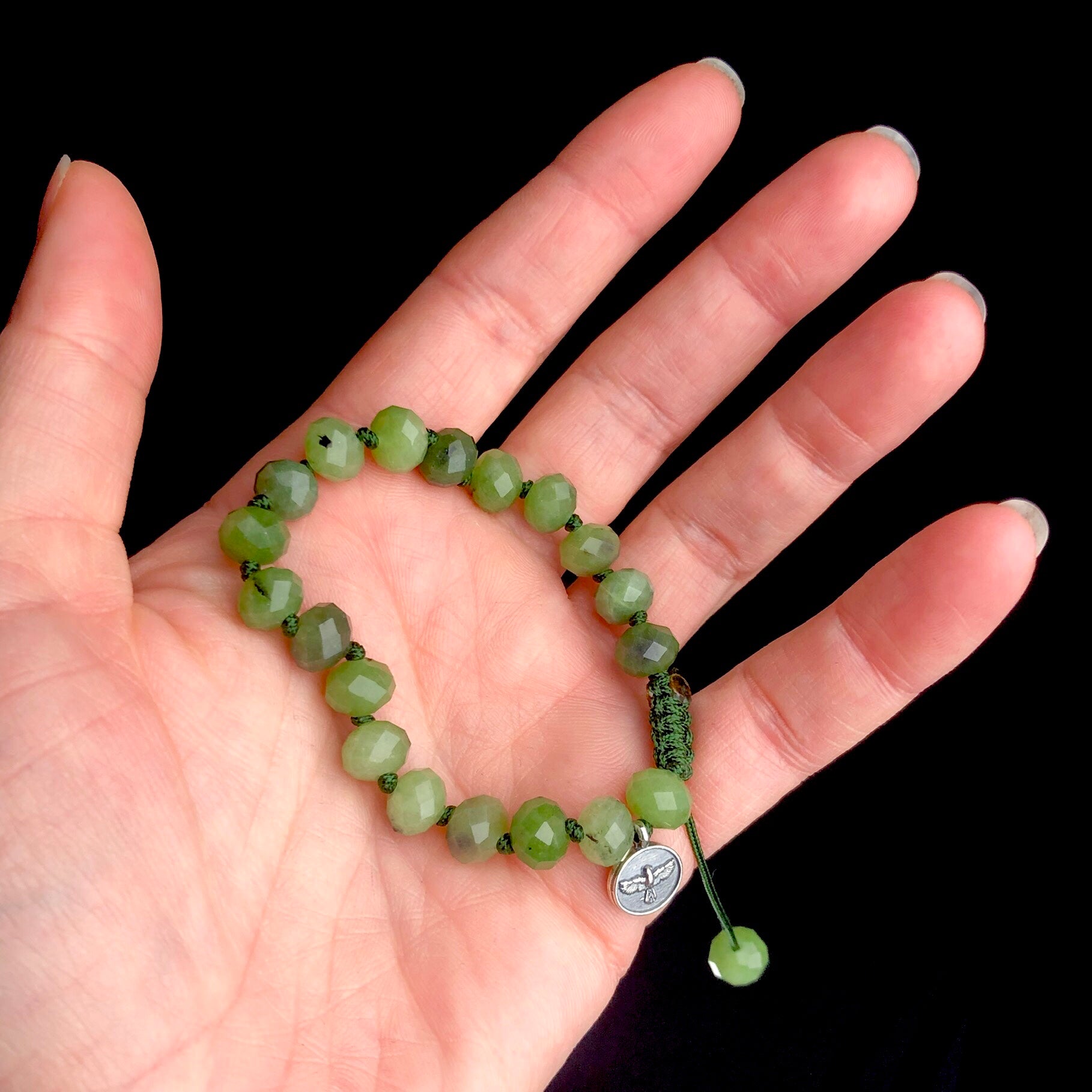 Opaque forest green colored bead bracelet knotted with dark green cord shown in hand