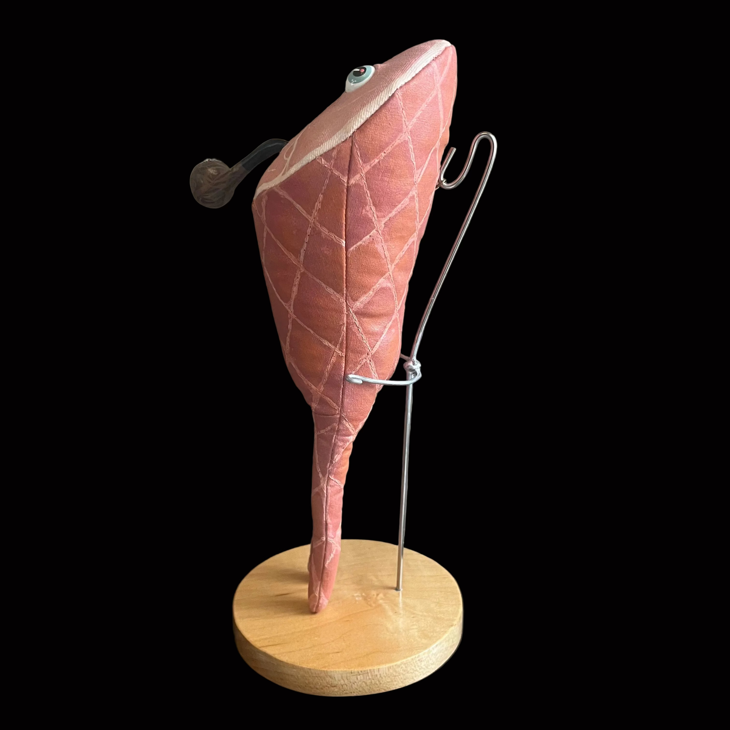 A pink quilted plush smoked ham food toy with a wooden base and metal display stand on a black background.