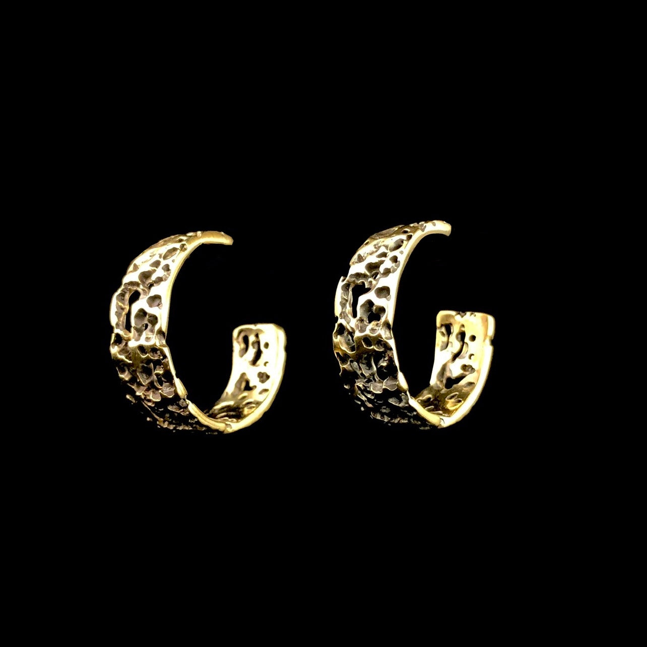 Front side view of Small Atoll Hoop Earrings with black background showing through textured brass