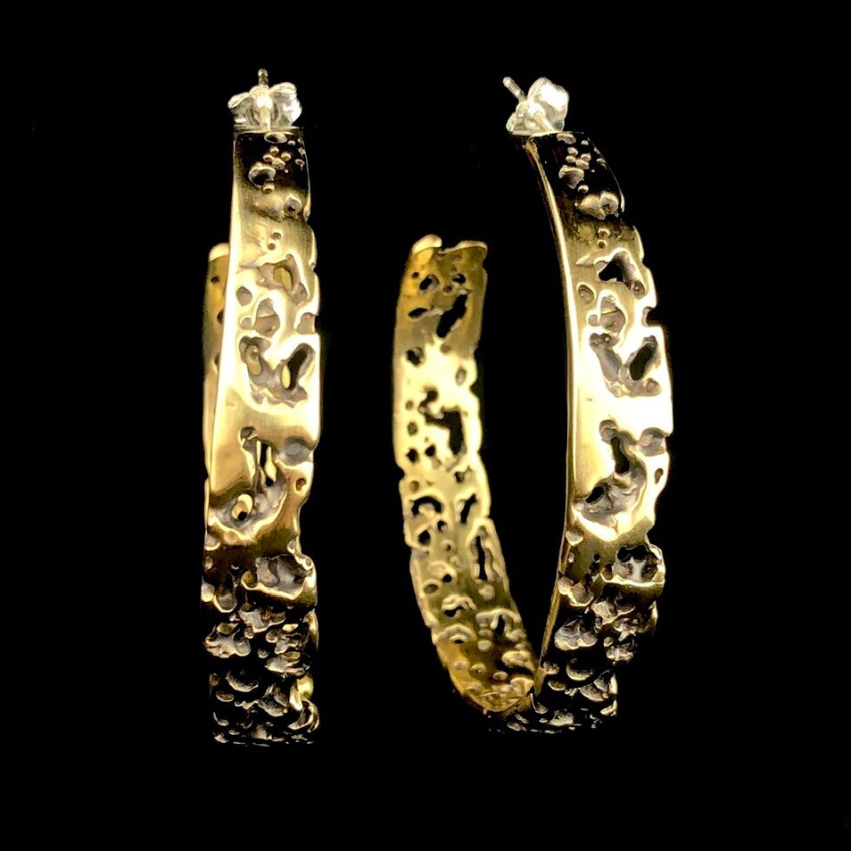 Front side view of Large Atoll Hoop Earrings with black background showing through textured brass 