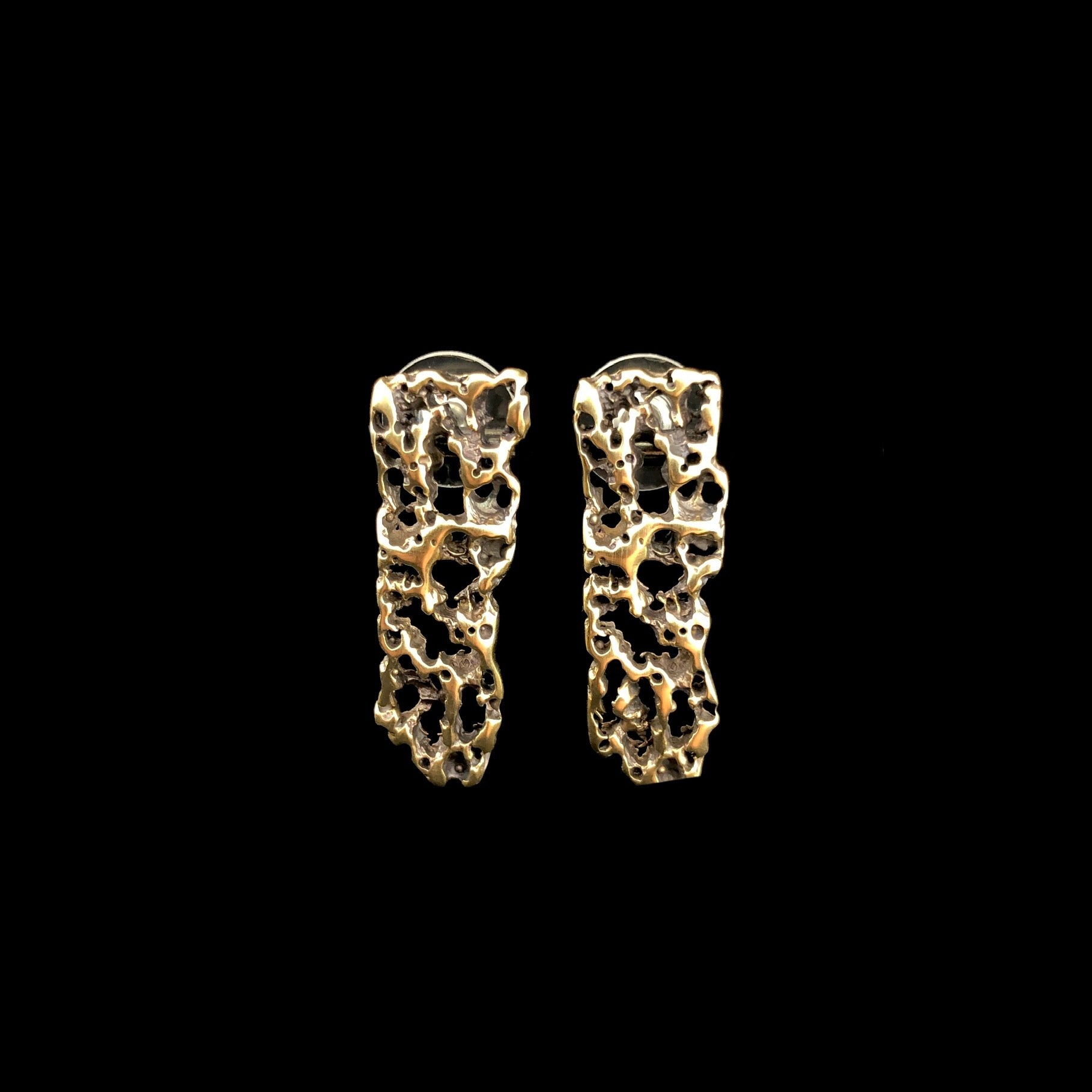 Front view of Short Atoll Vertical Earrings with black background showing through textured brass