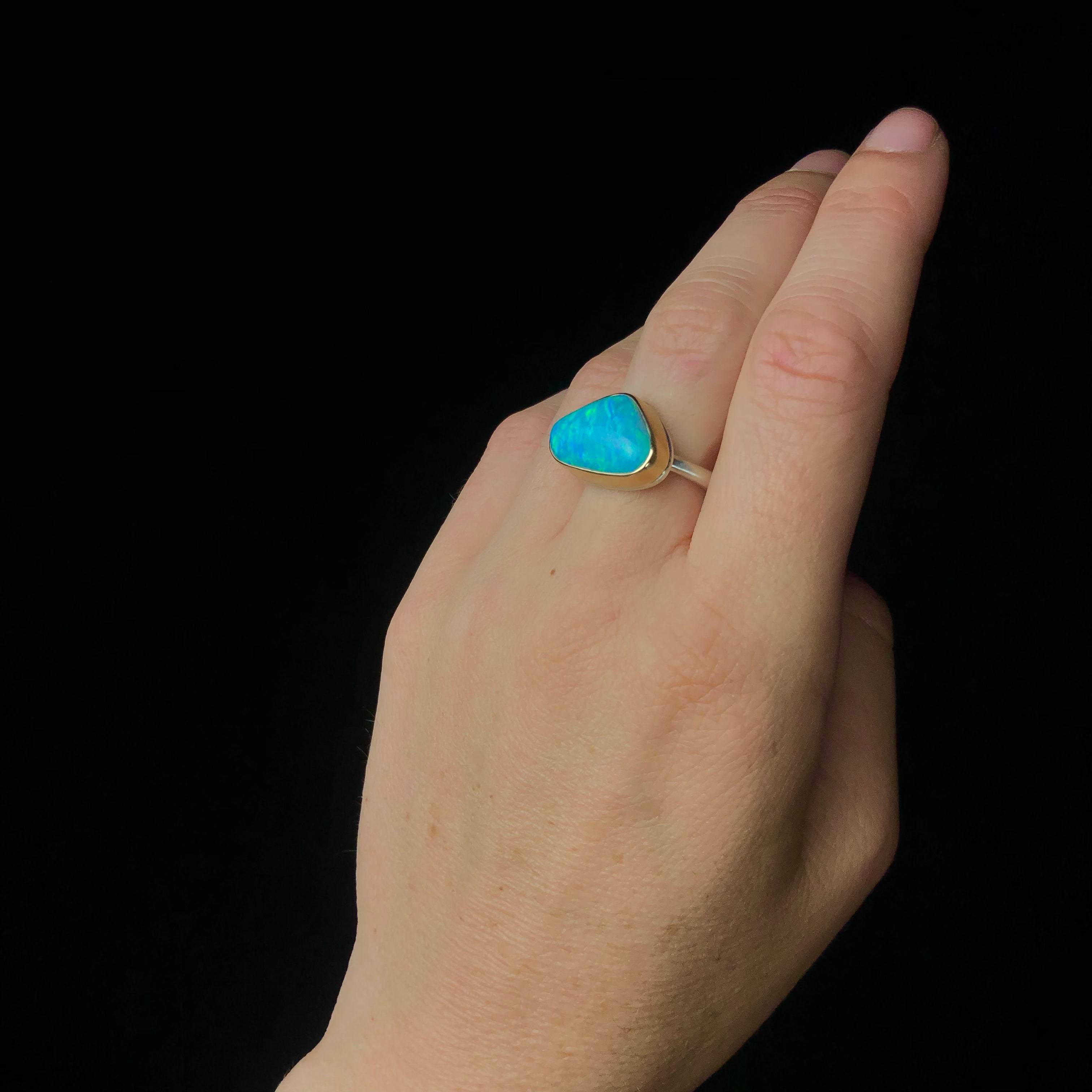 Side view with gold set green and blue opal stone mounted on silver band shown worn on hand