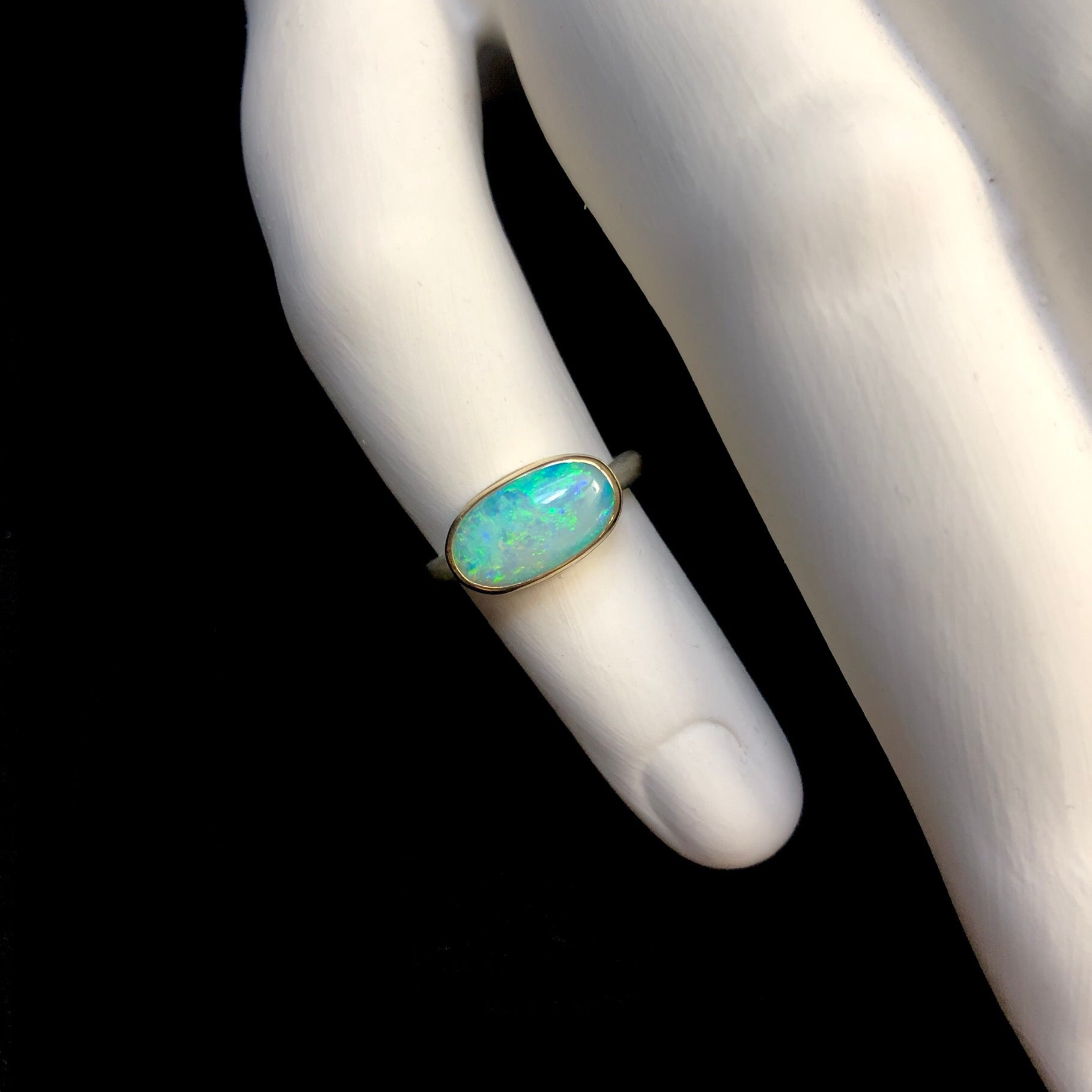 Oval shaped light green and blue opal stone ring shown on white ceramic finger