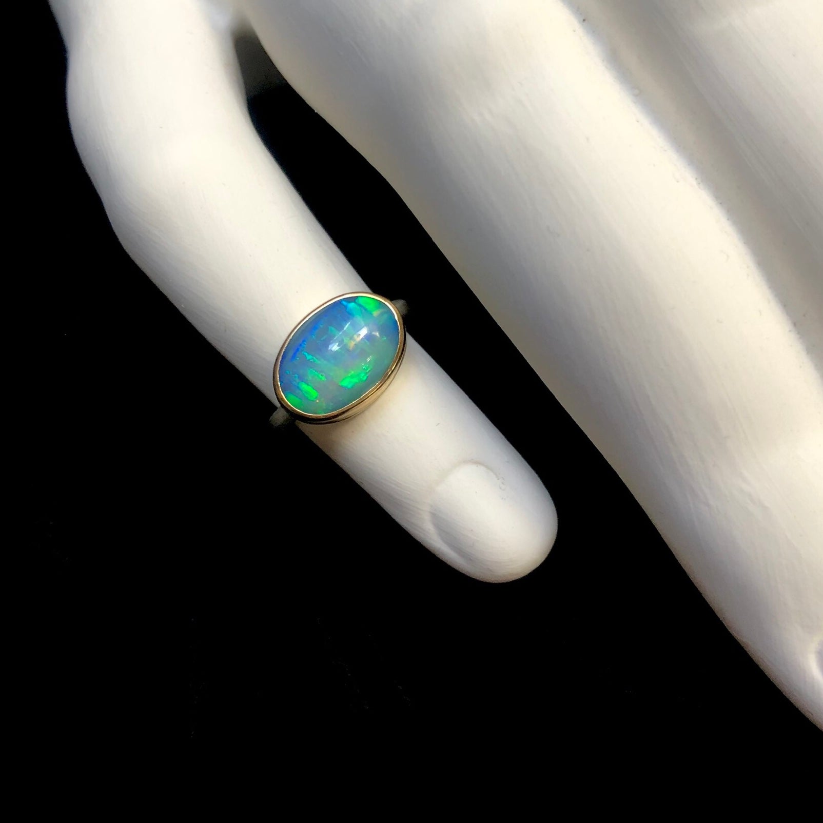 Oval shaped blue and green opal stone ring shown on white ceramic hand