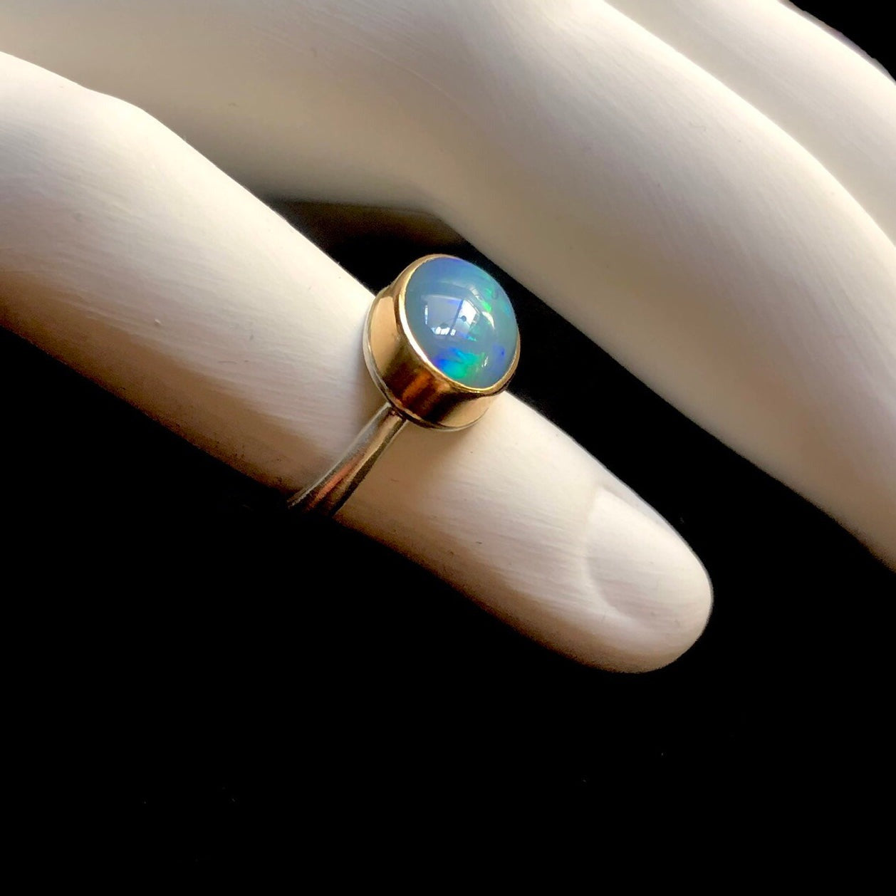 Profile side view of smooth blue opal stone with gold setting and silver band shown on white ceramic finger
