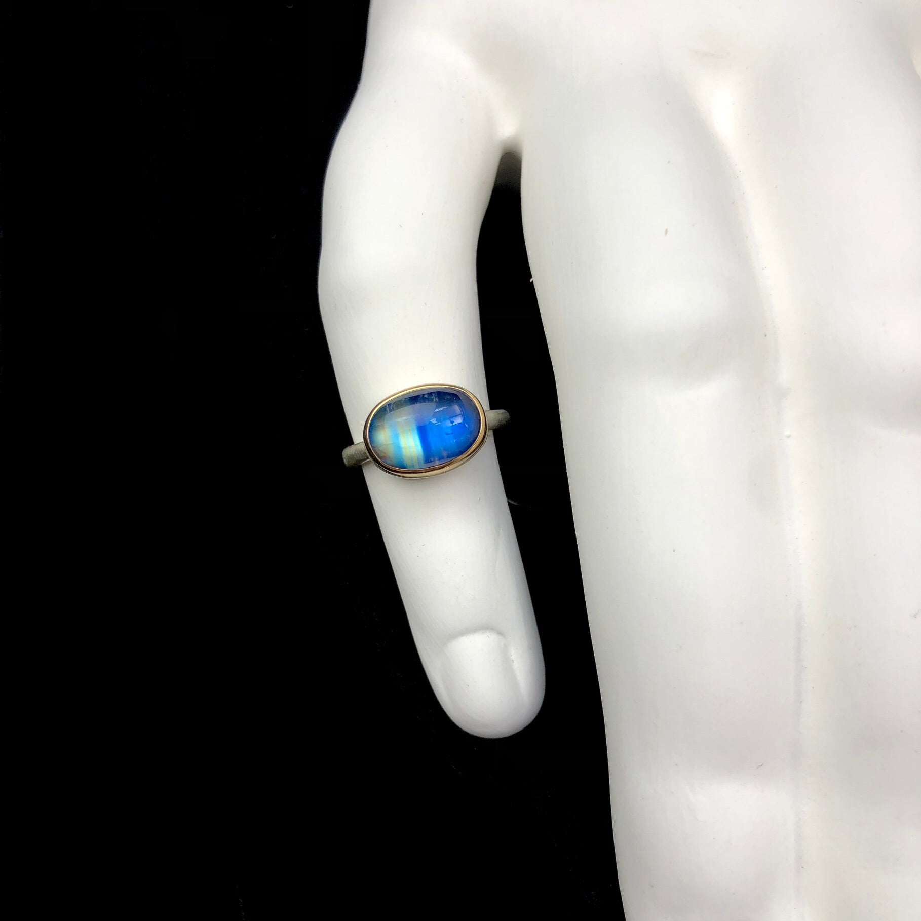 Top view of Oval Rianbow Moonstone Ring shown on white ceramic finger