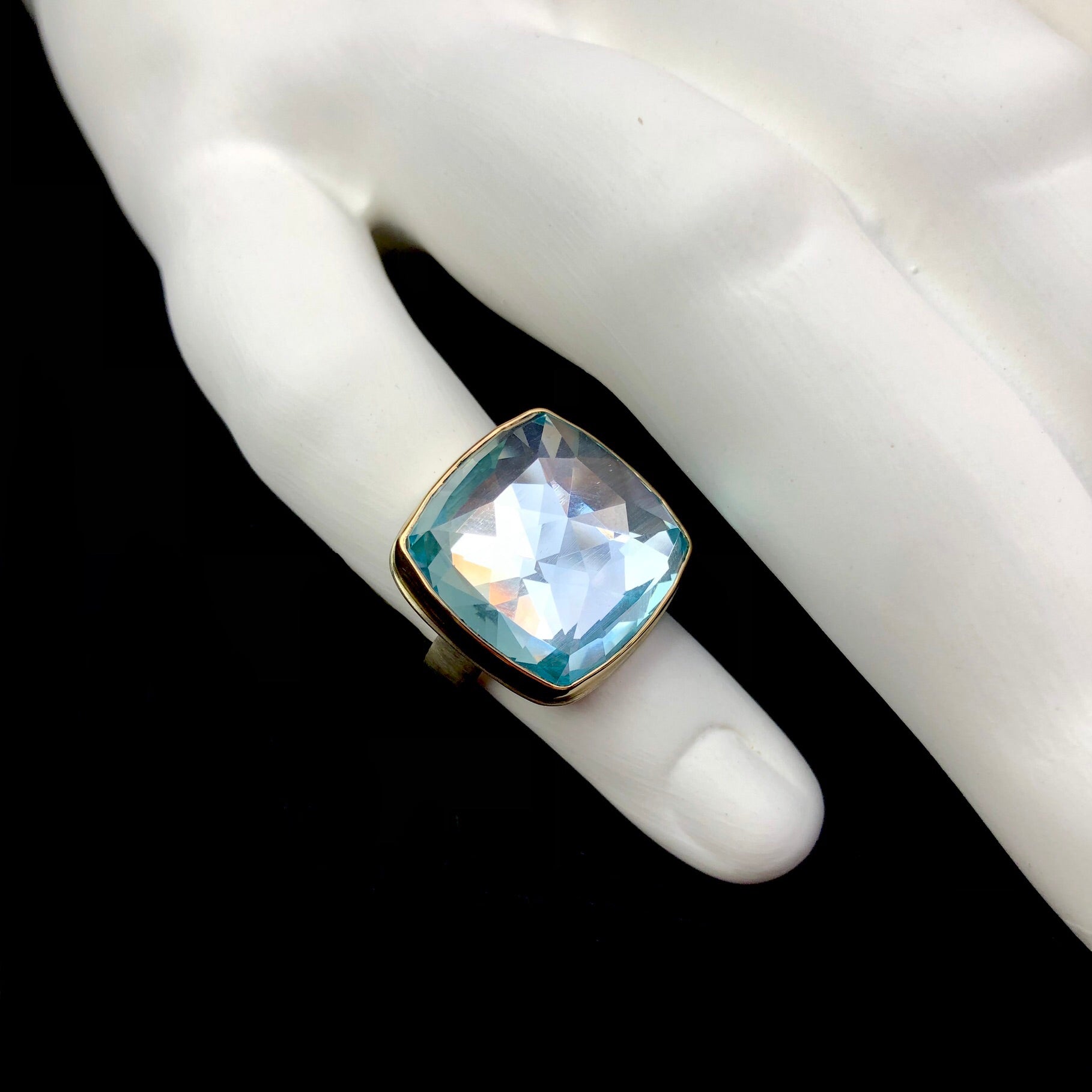 Top view of Square shaped Sky Blue Topaz ring with light captured inside shown on white ceramic finger