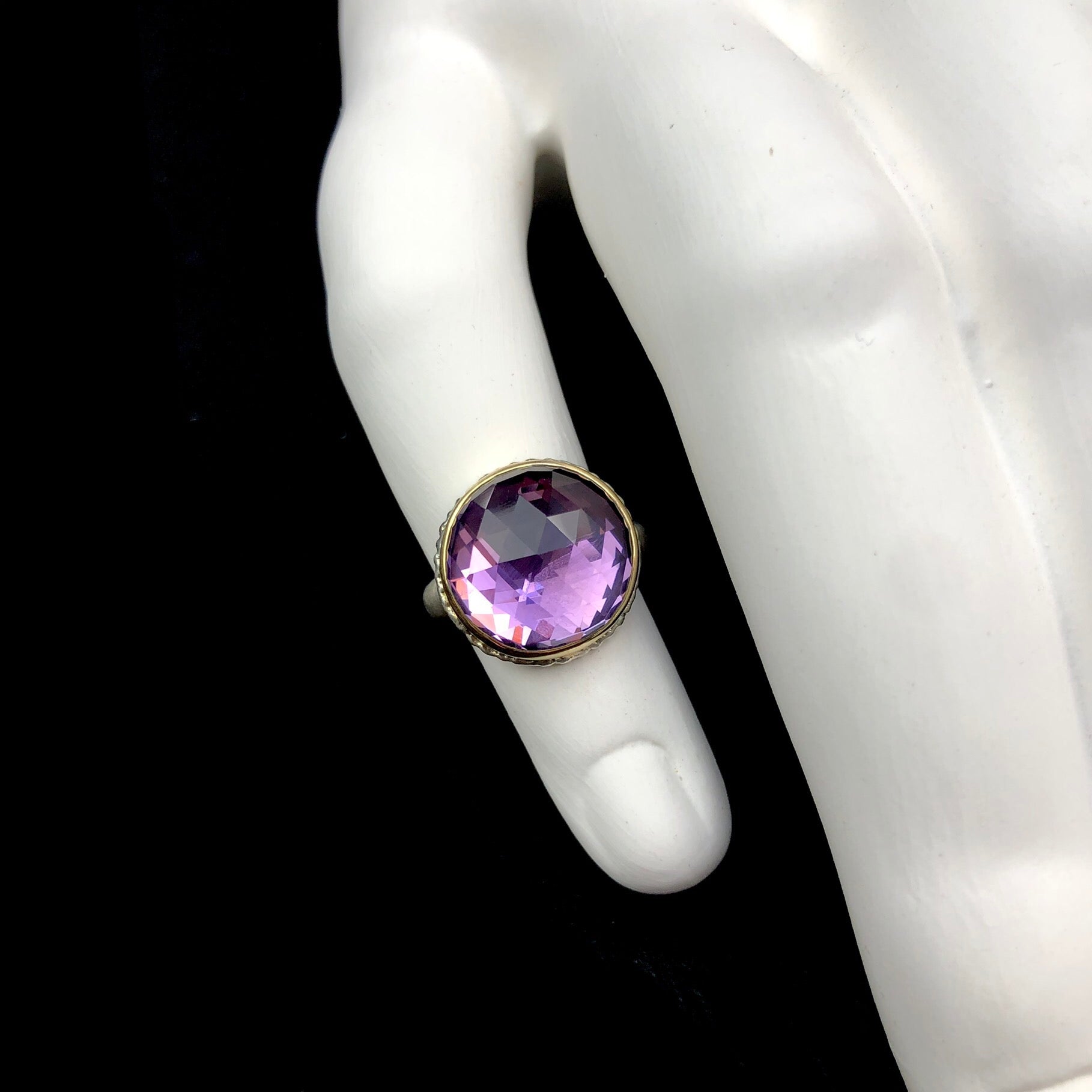 Round checkerboard cut purple stone shown on white ceramic finger