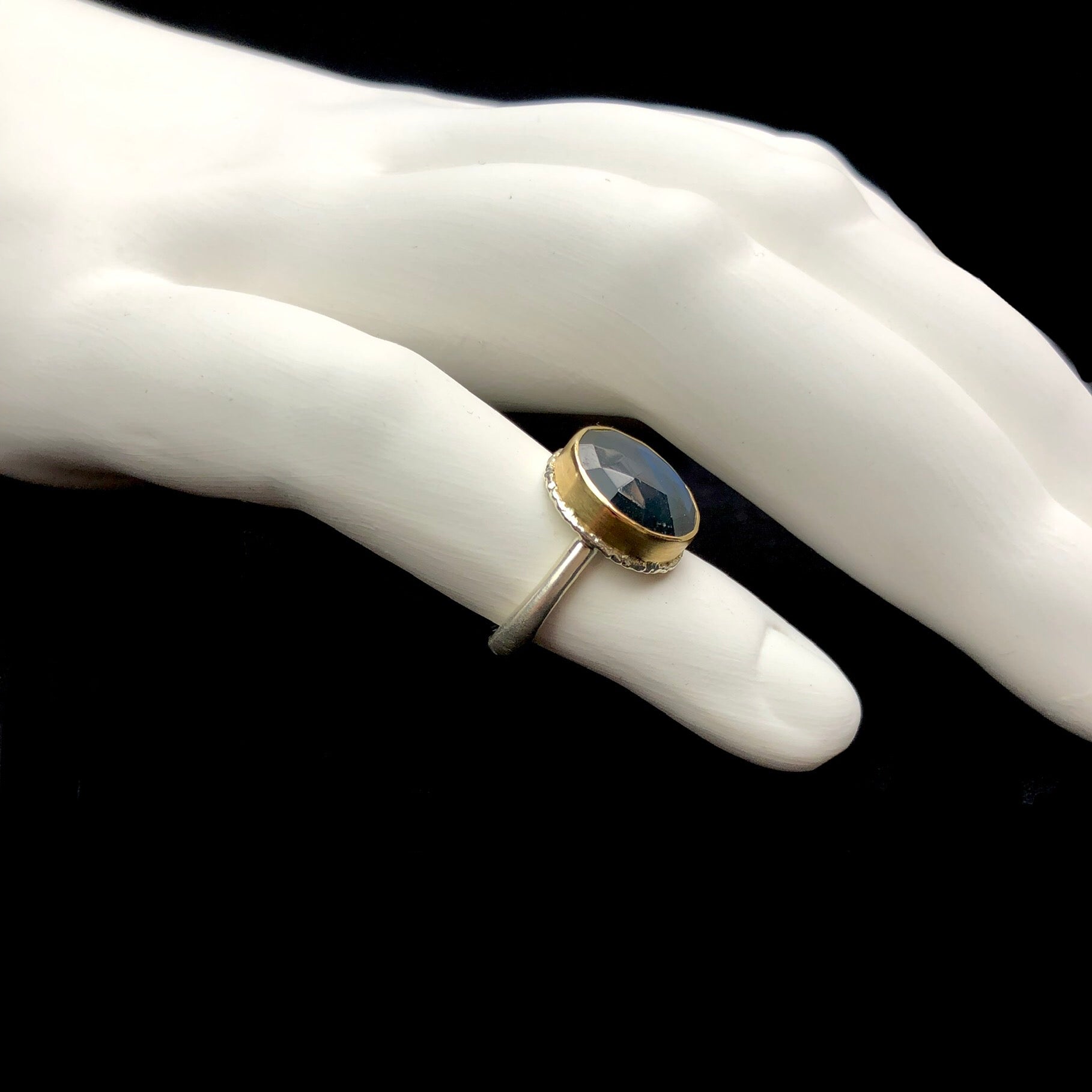 Side view of stone ring with gold setting and silver band shown on white ceramic finger