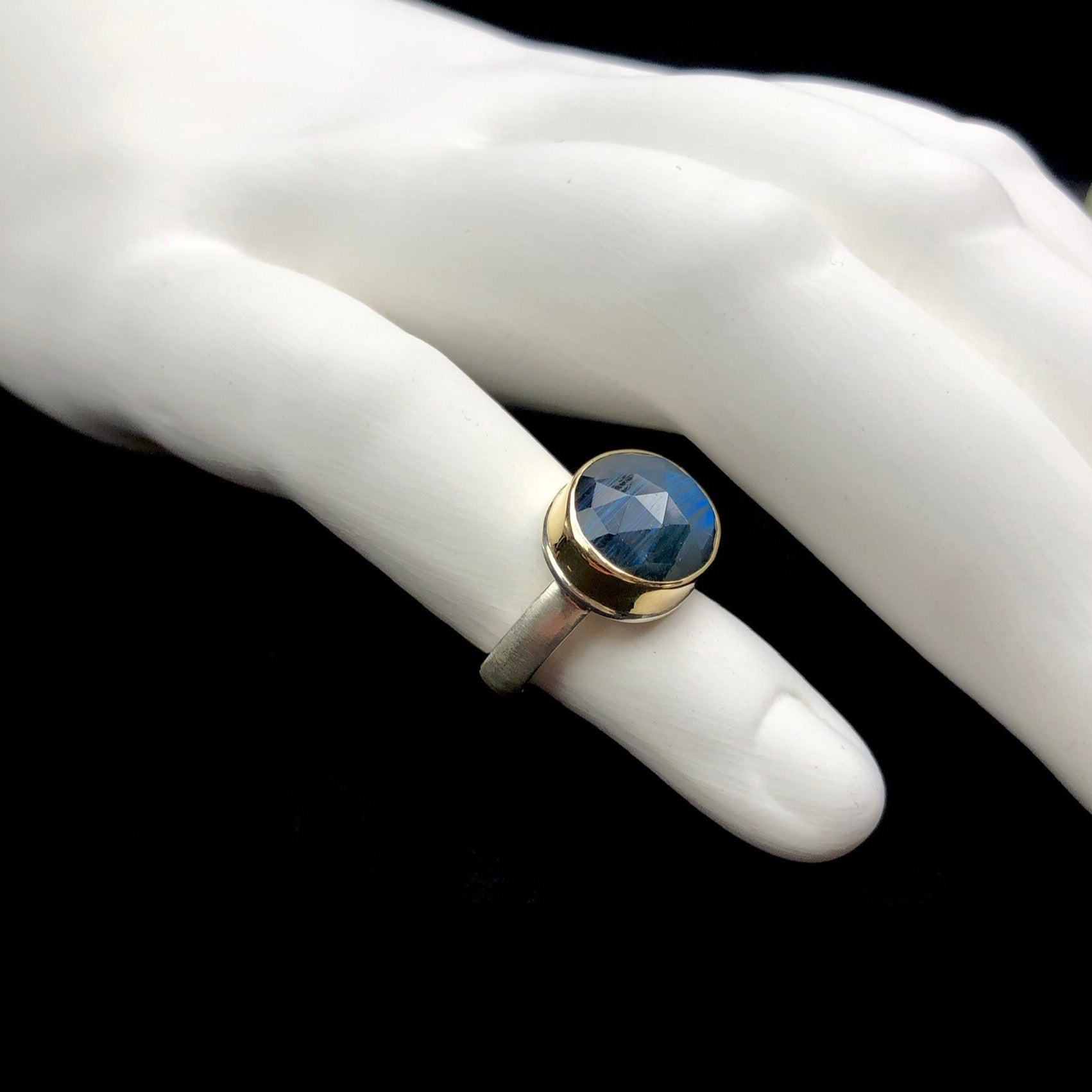 Side profile view of cut stone surface with gold setting and silver band on white ceramic finger