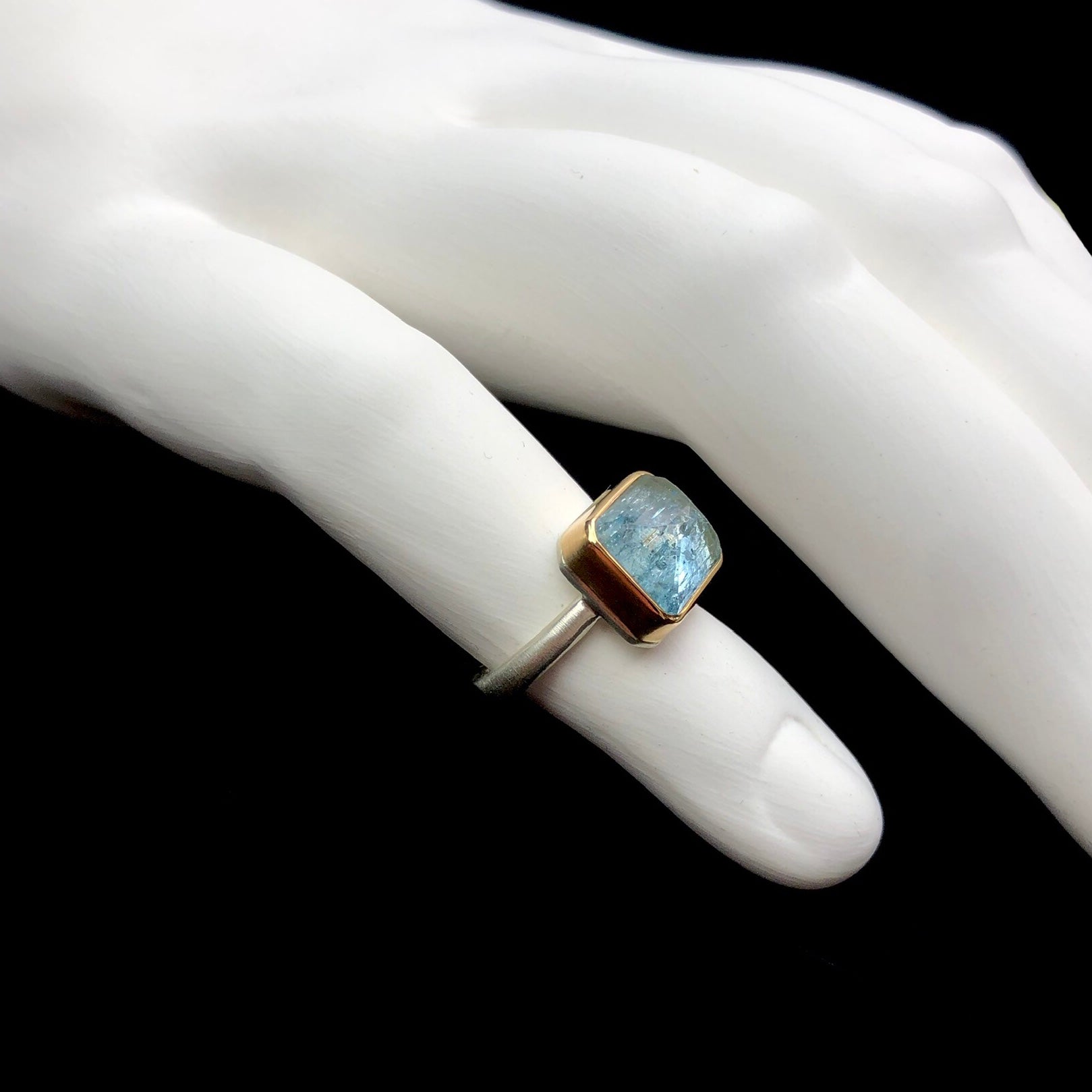 Side profile view of aquamarine stone ring with gold setting and silver band on white ceramic finger