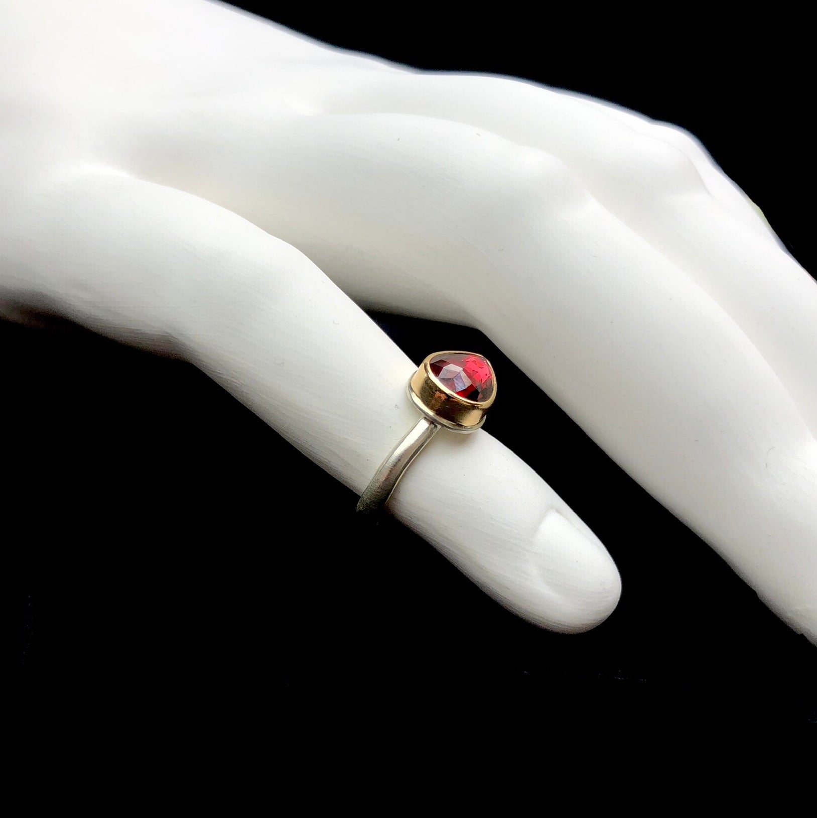 Side view of red colored garnet stone ring with gold setting and silver band shown on white ceramic finger