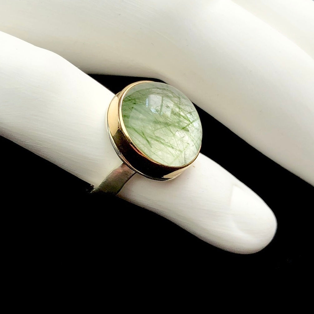 Side profile view of smooth, rounded light green stone ring on white ceramic finger