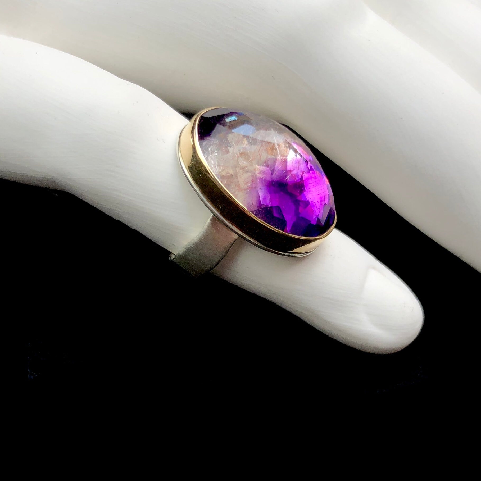 Side profile view of faceted pyramid shape of clear and purple stone ring shown on white ceramic finger