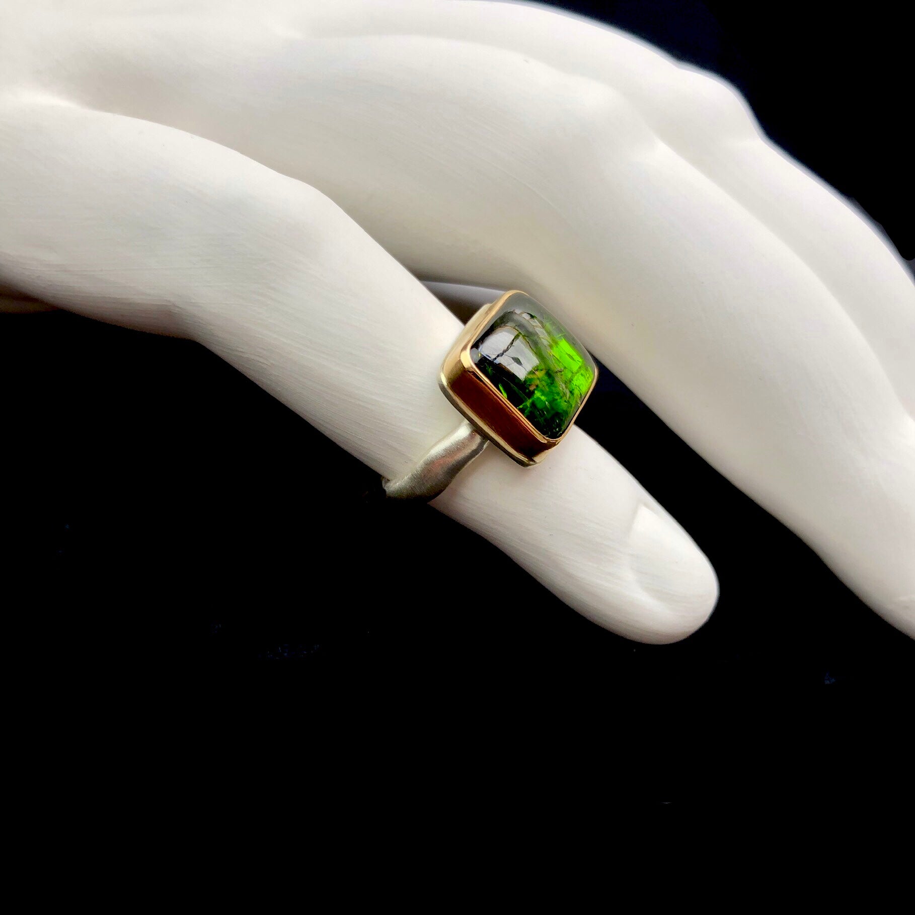 Side profile view of Green Tourmaline Ring with gold setting and silver band shown on white ceramic finger