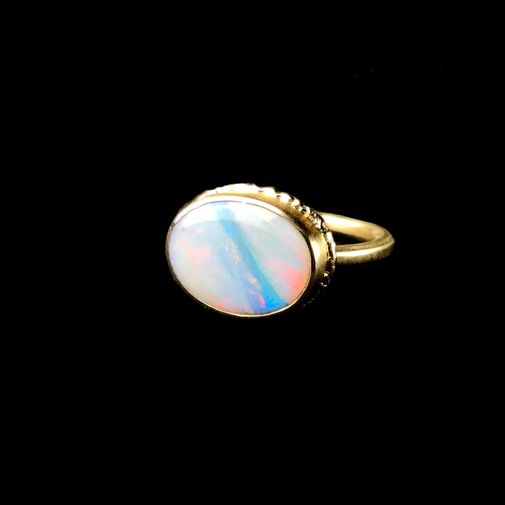 White iridescent opal stone with blue band running diagonally across it set in solid gold ring