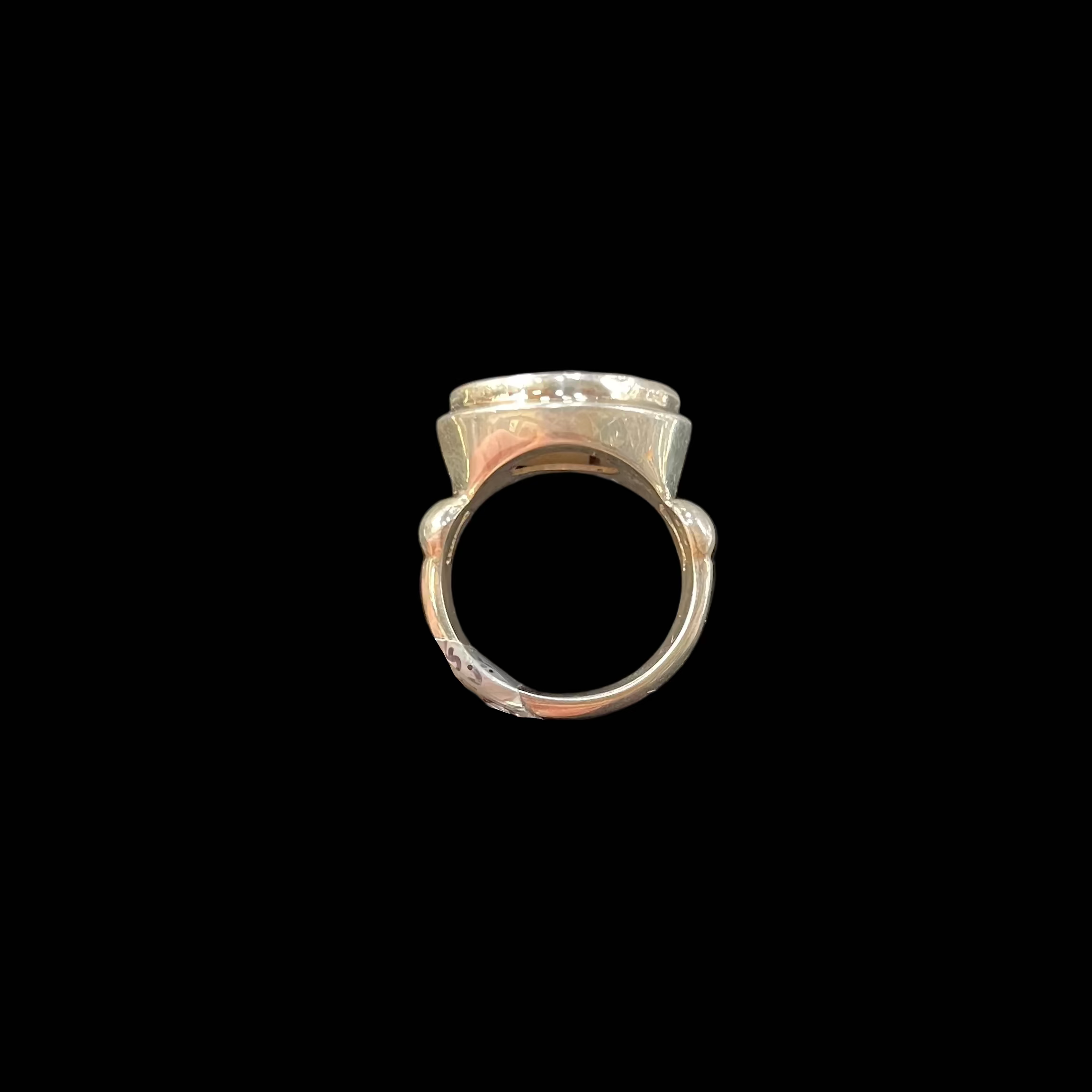 Silver ring held between thumb and forefinger against a black background