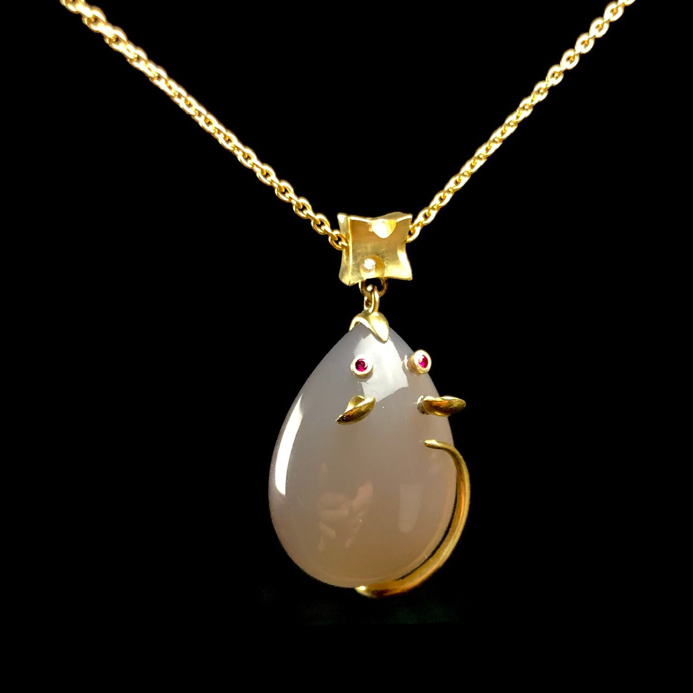 Close up view of smooth stone body of mouse pendant on gold chian