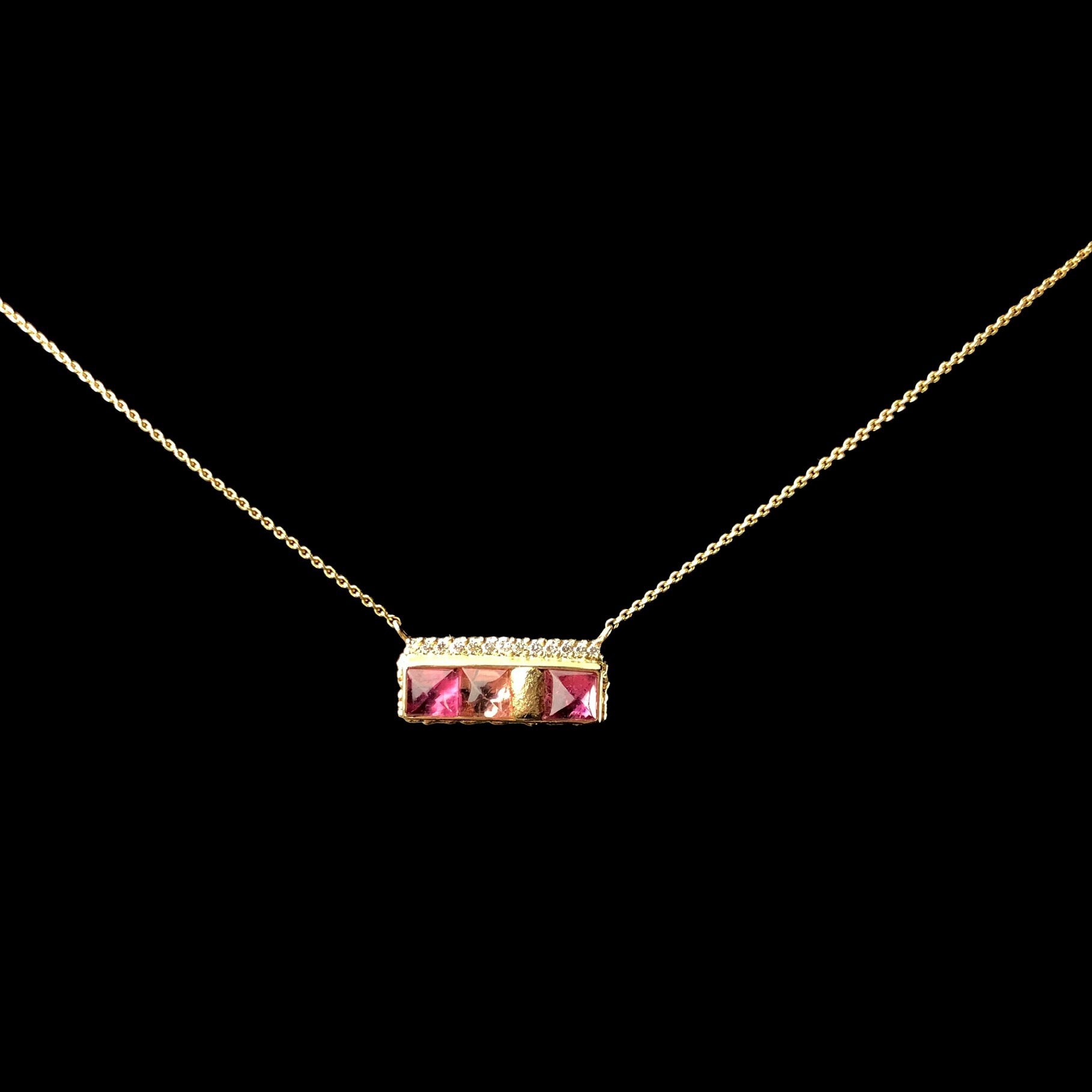 Three different hues of pink tourmaline stones glow in a ruffled gold setting on chain 