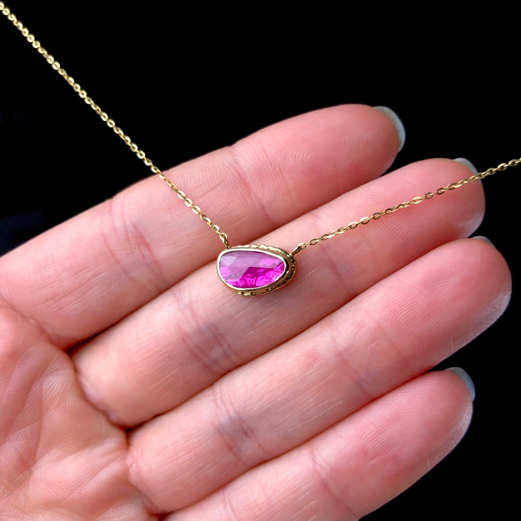 Pink stone necklace on gold chain shown agains hand