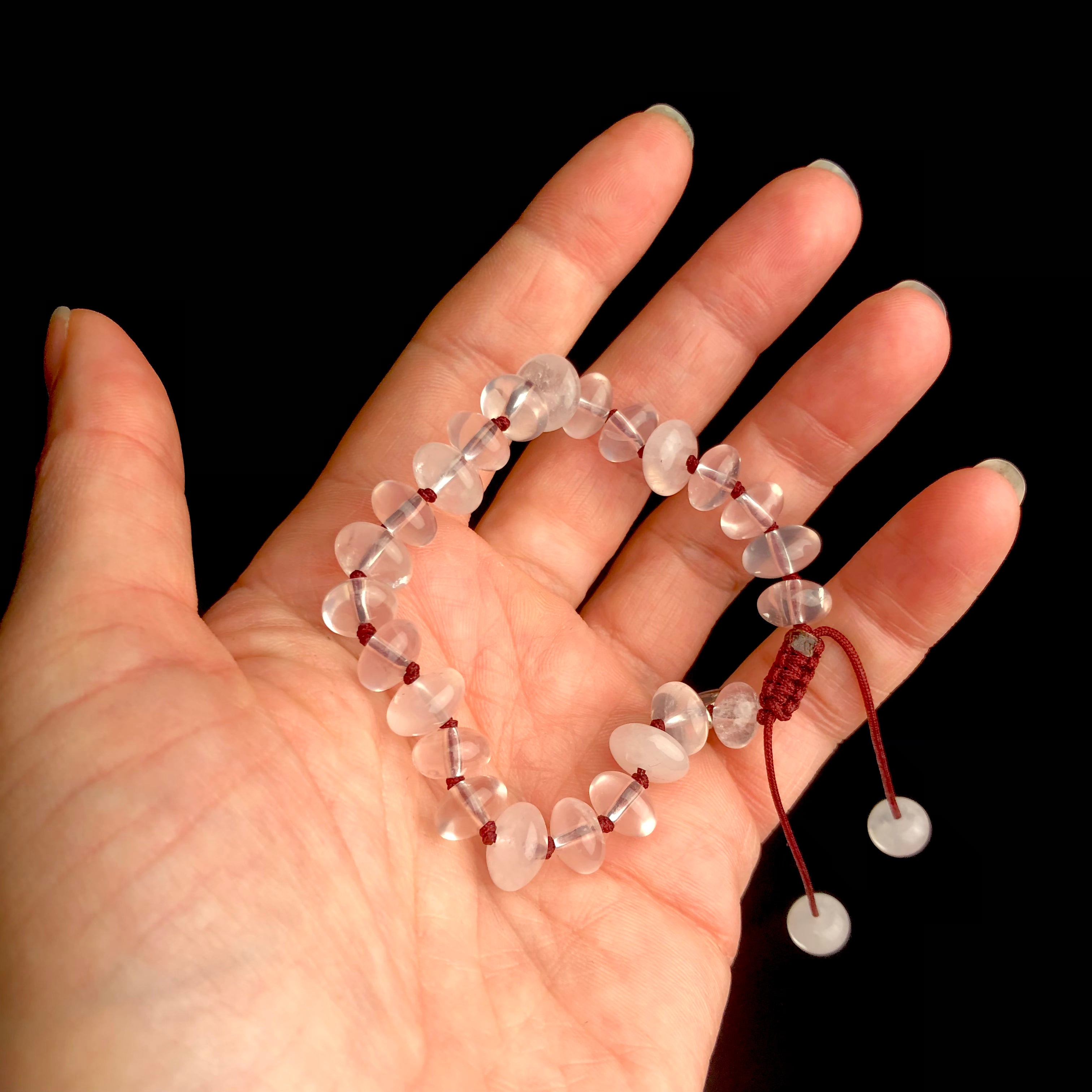 Translucent light pink colored stone bracelet on dark red knotted cord shown in hand