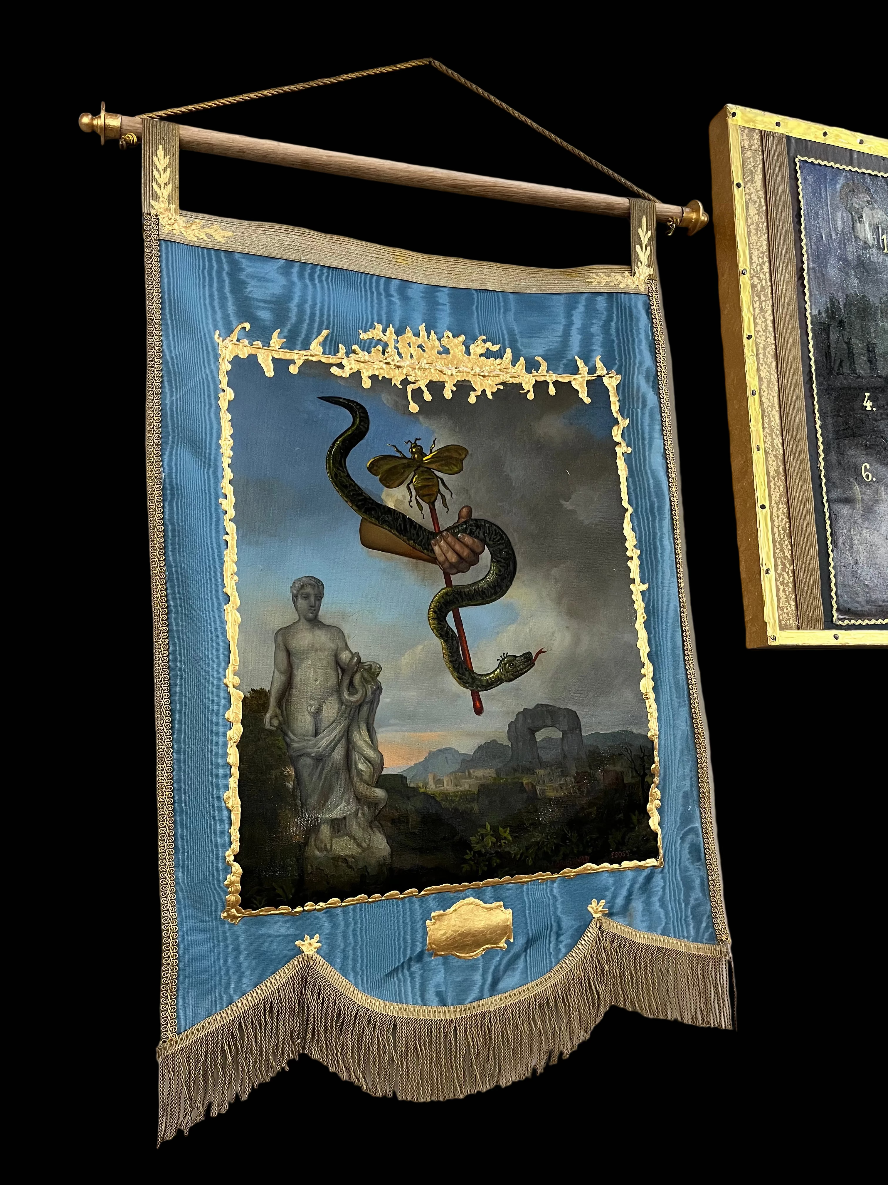 Decorative banner with classical design featuring a snake and statue, framed in gold on a wall.