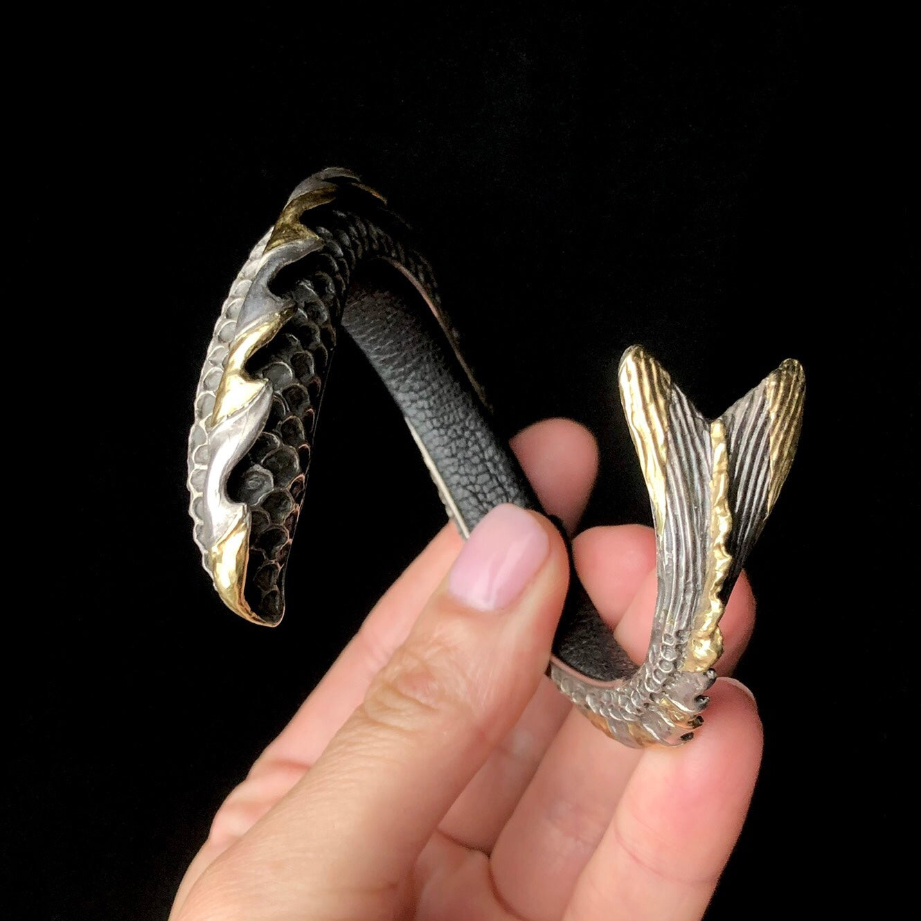 Hand holding spring shaped silver bracelet with fish-like tail design on black background