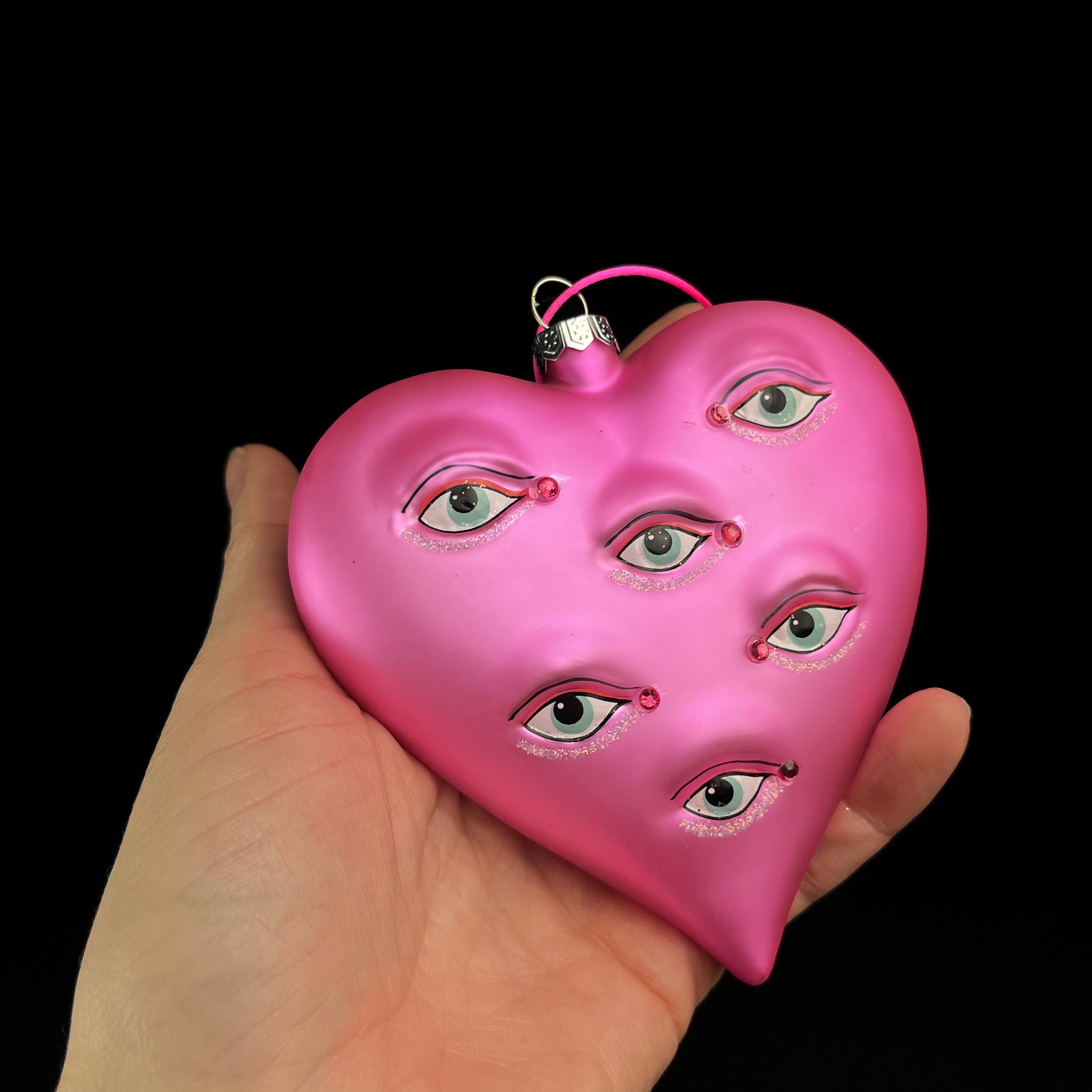 Pink heart-shaped object with face details held in a hand against a black background
