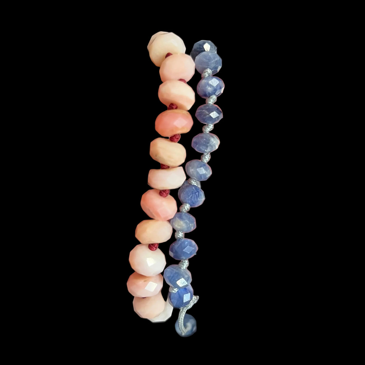 Two beaded bracelets held in a hand. One bracelet features round off-white beads, and the other features faceted blue beads, both separated by small red spacer beads.