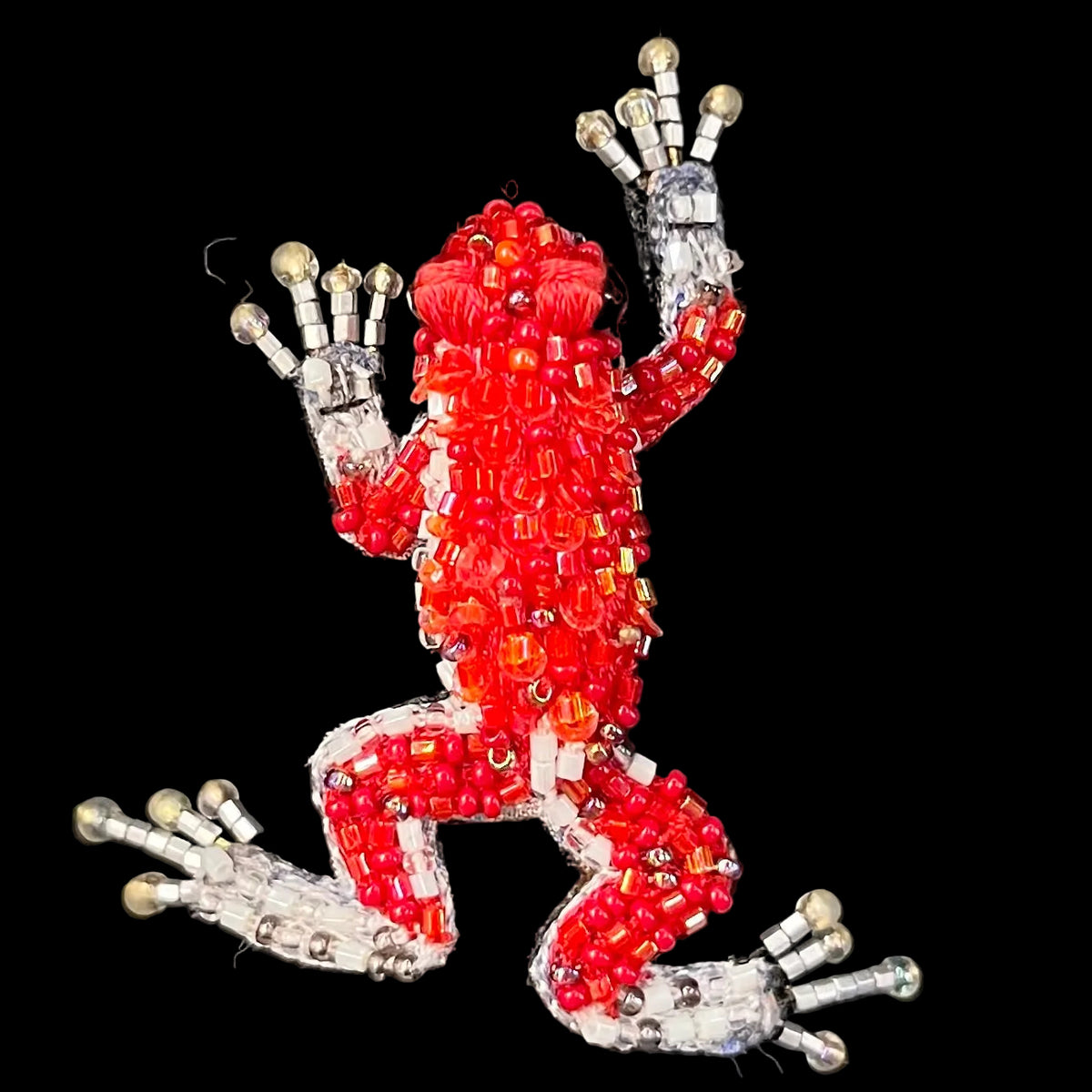 A frog-shaped brooch or pin made from red and orange seed beads with silver-toned metal accents, shown on a black background.