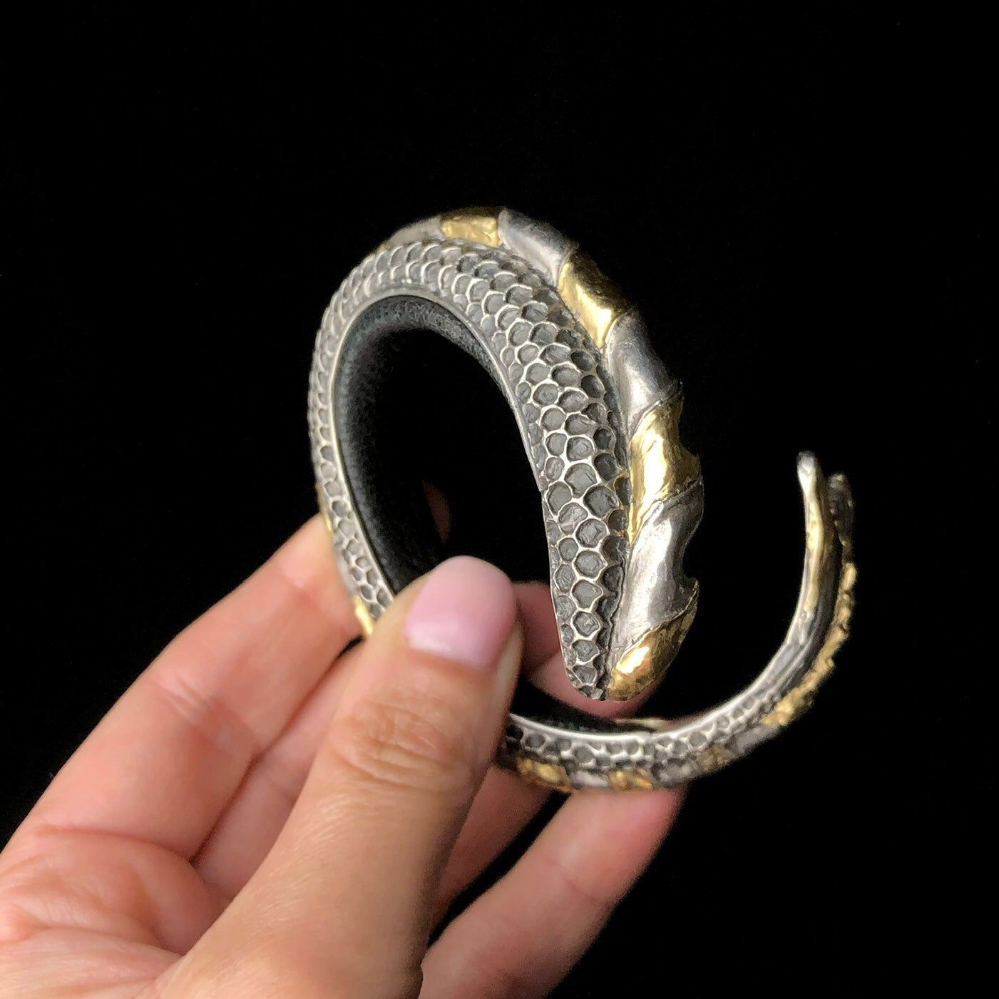Hand golding silver and gold bracelet with scale-like design.