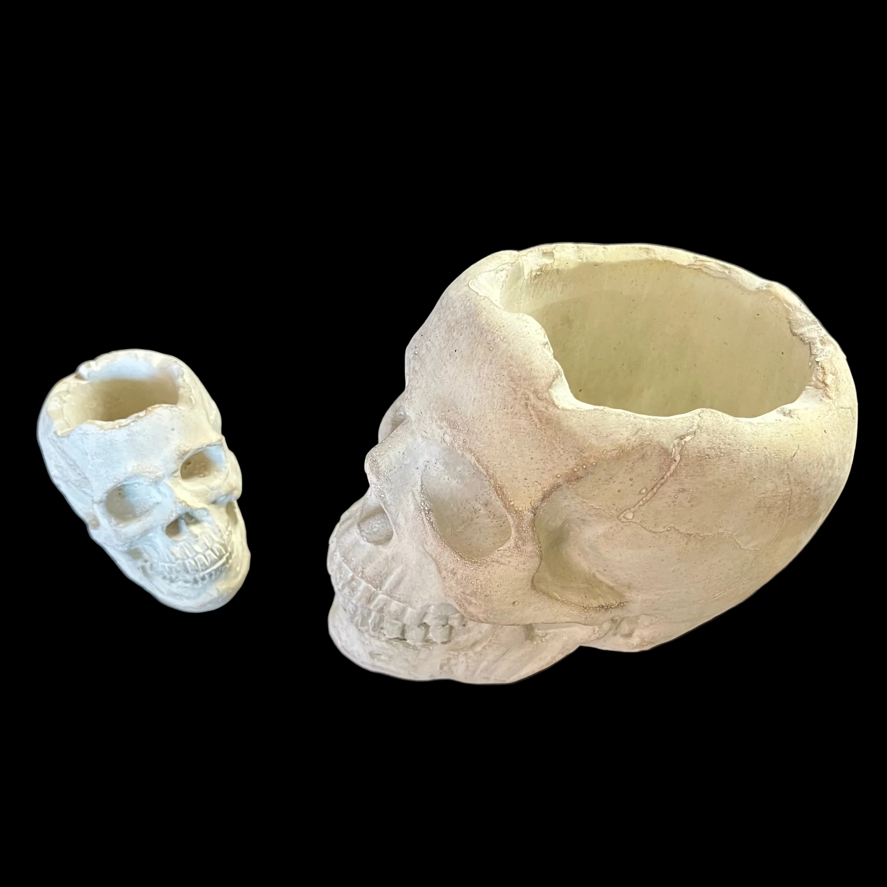 Two skull-shaped ceramic pots on a black surface