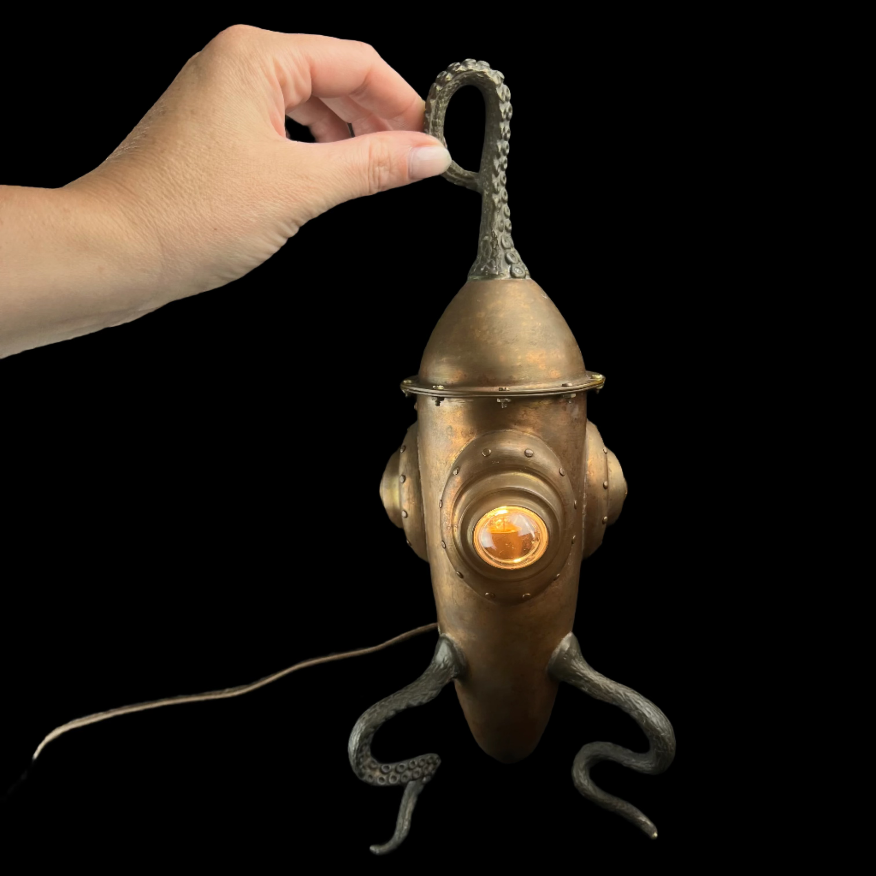 Decorative metal squid lamp with a hand holding it against a dark background