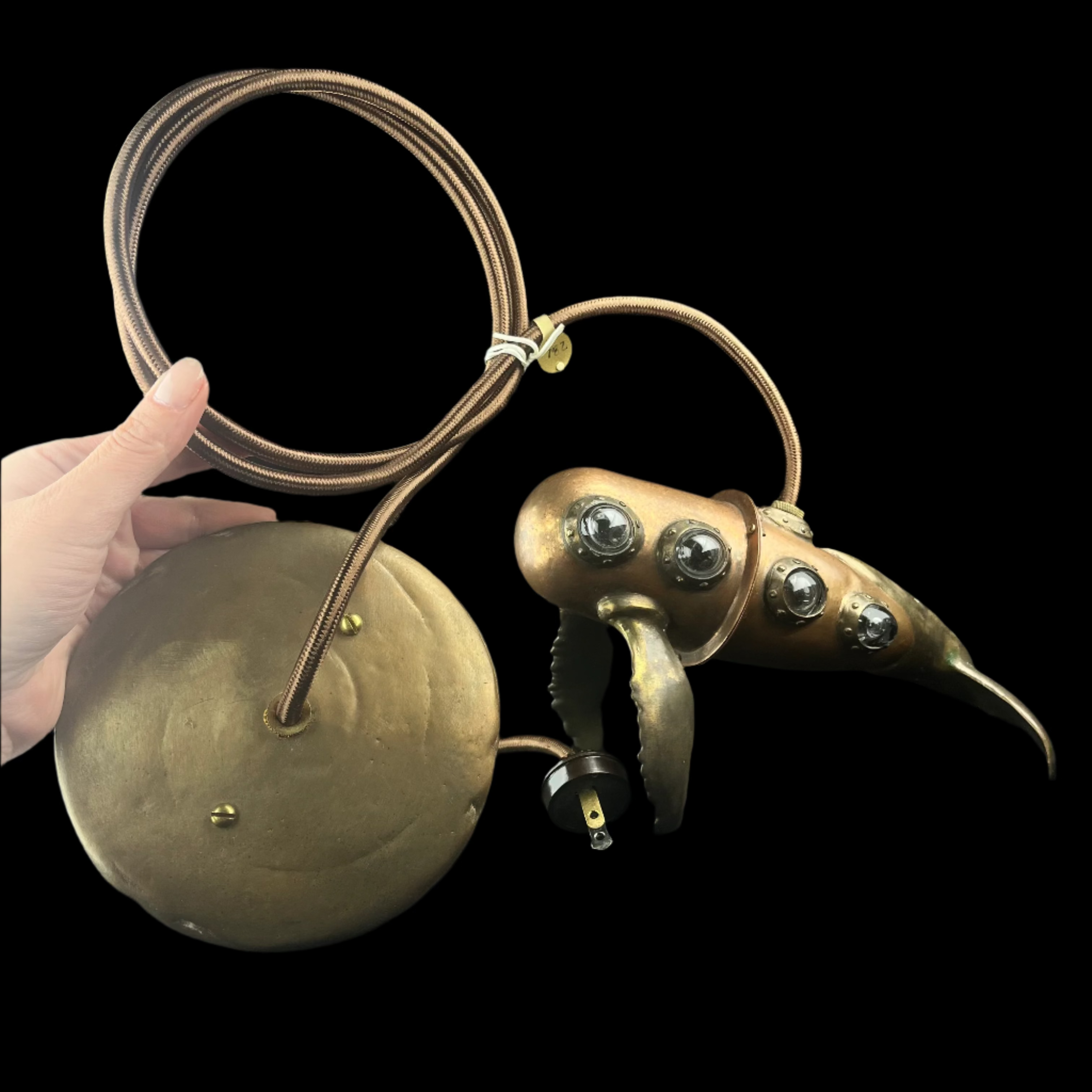 Brass bird-shaped object with a round base held by a hand on a dark surface.