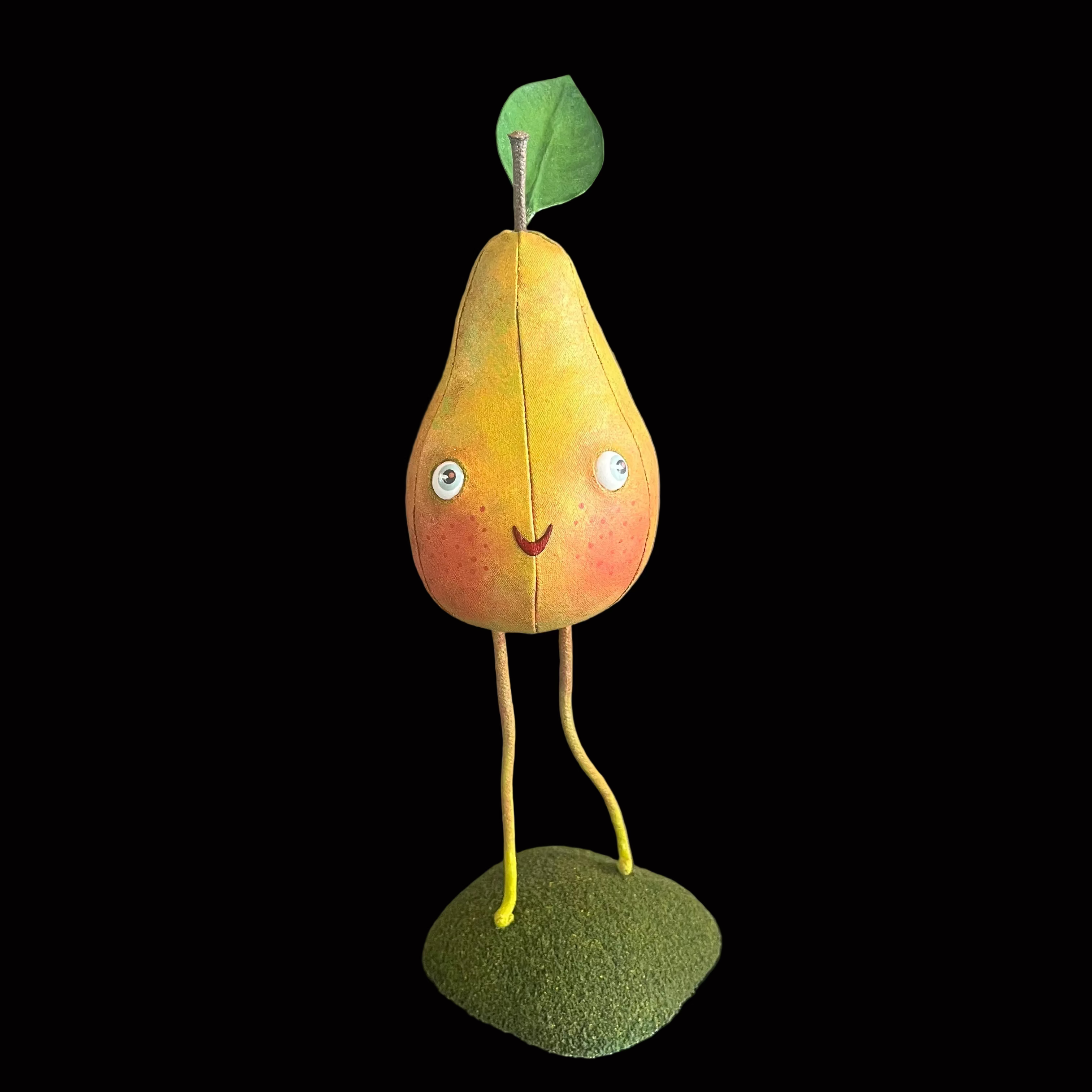 Whimsical vegetable-shaped decorative figure standing on mossy bases against black background resembling a yellow pear with green leave and a smiling face.