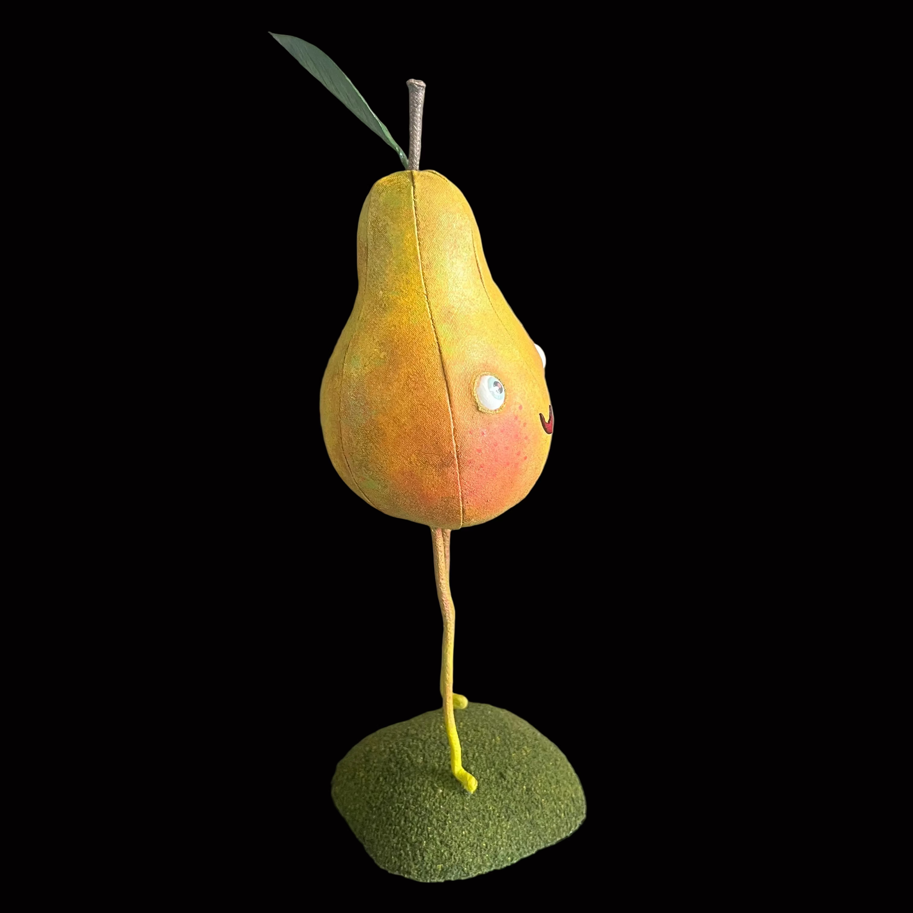 Whimsical vegetable-shaped decorative figure standing on mossy bases against black background resembling a yellow pear with green leave and a smiling face.