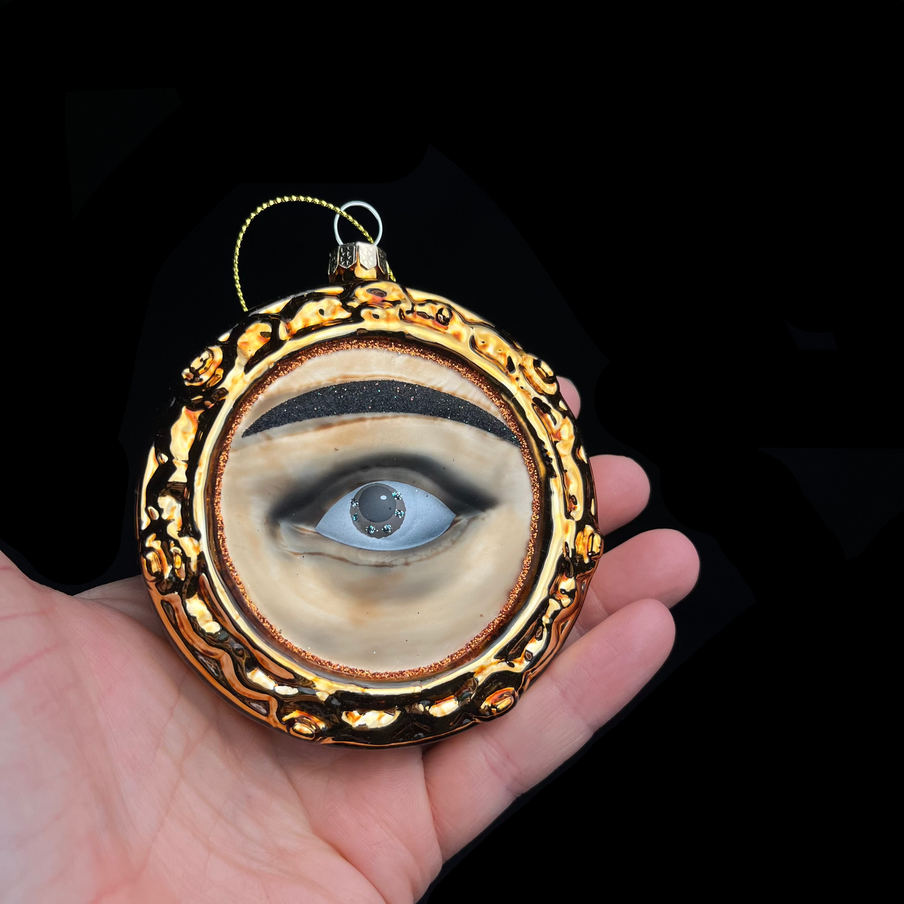 Decorative ornament with an eye design held in a hand against a black background
