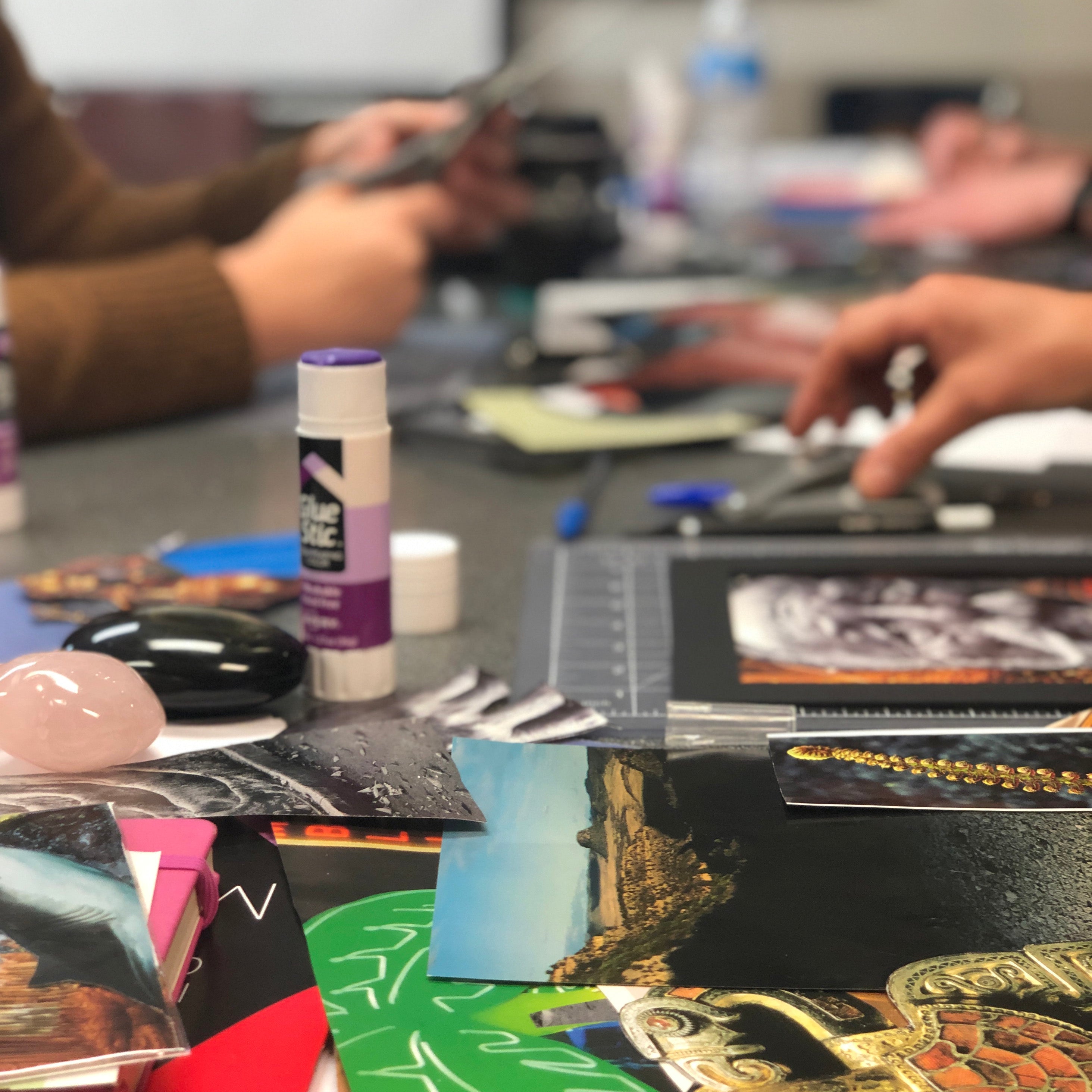 Art supplies and materials on a table with people working in the background